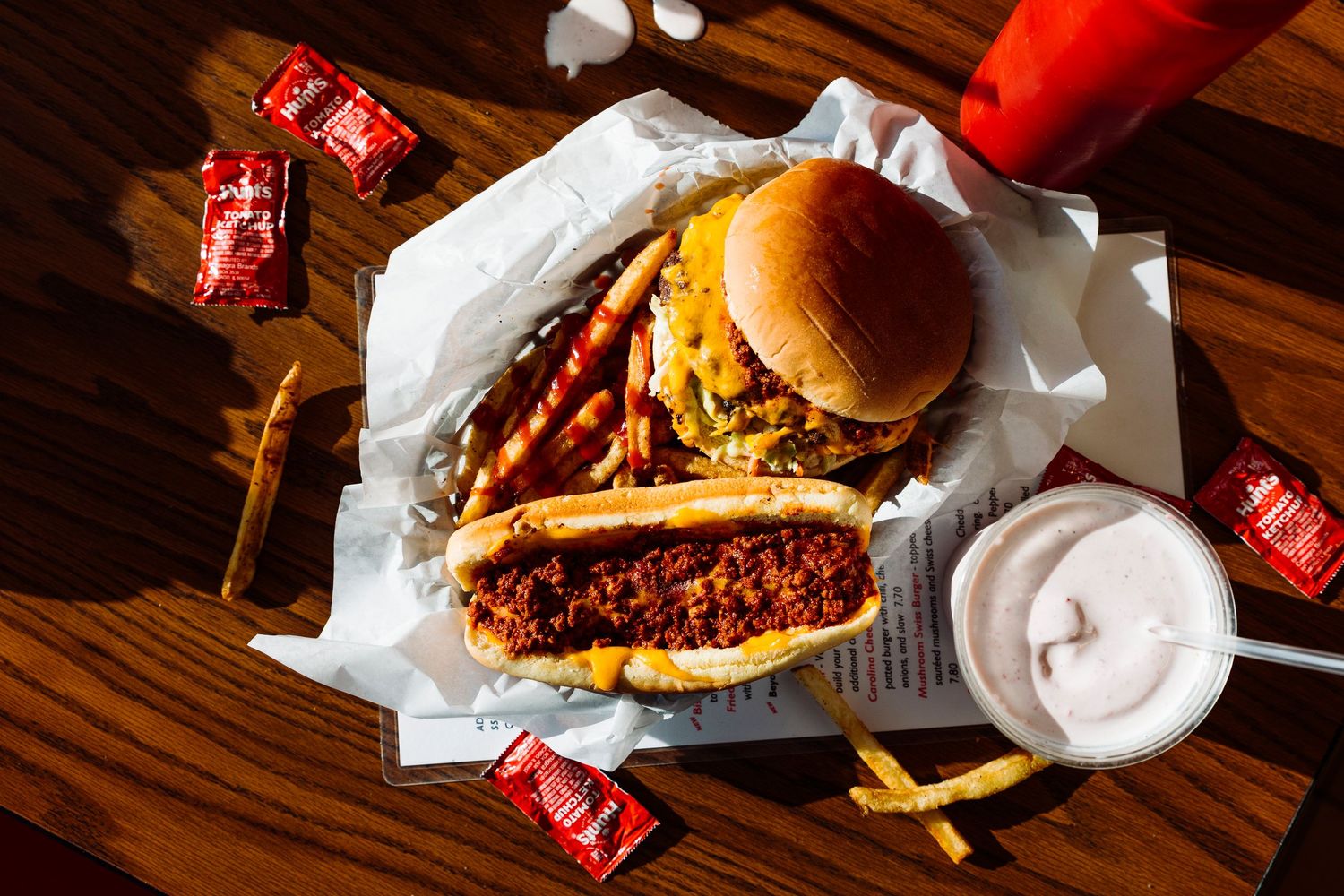 Juicy cheeseburger with fries and milkshake served with hot sauce packets on wooden table.