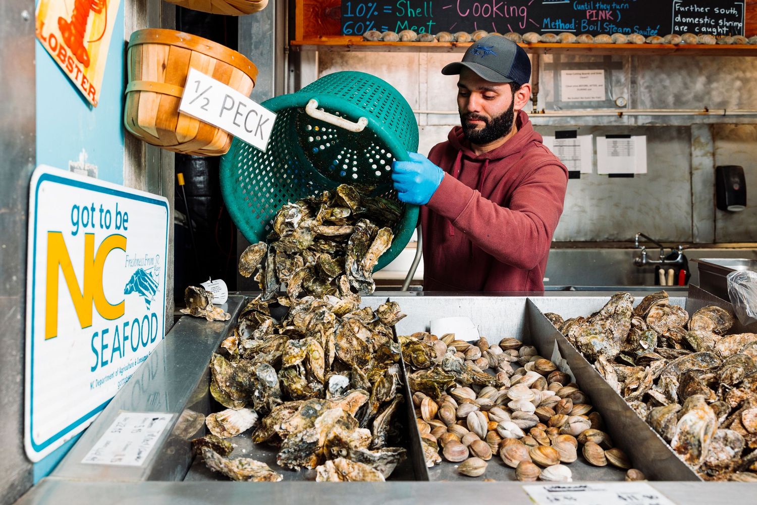 Worker pouring fresh oysters into display bins at a seafood market.