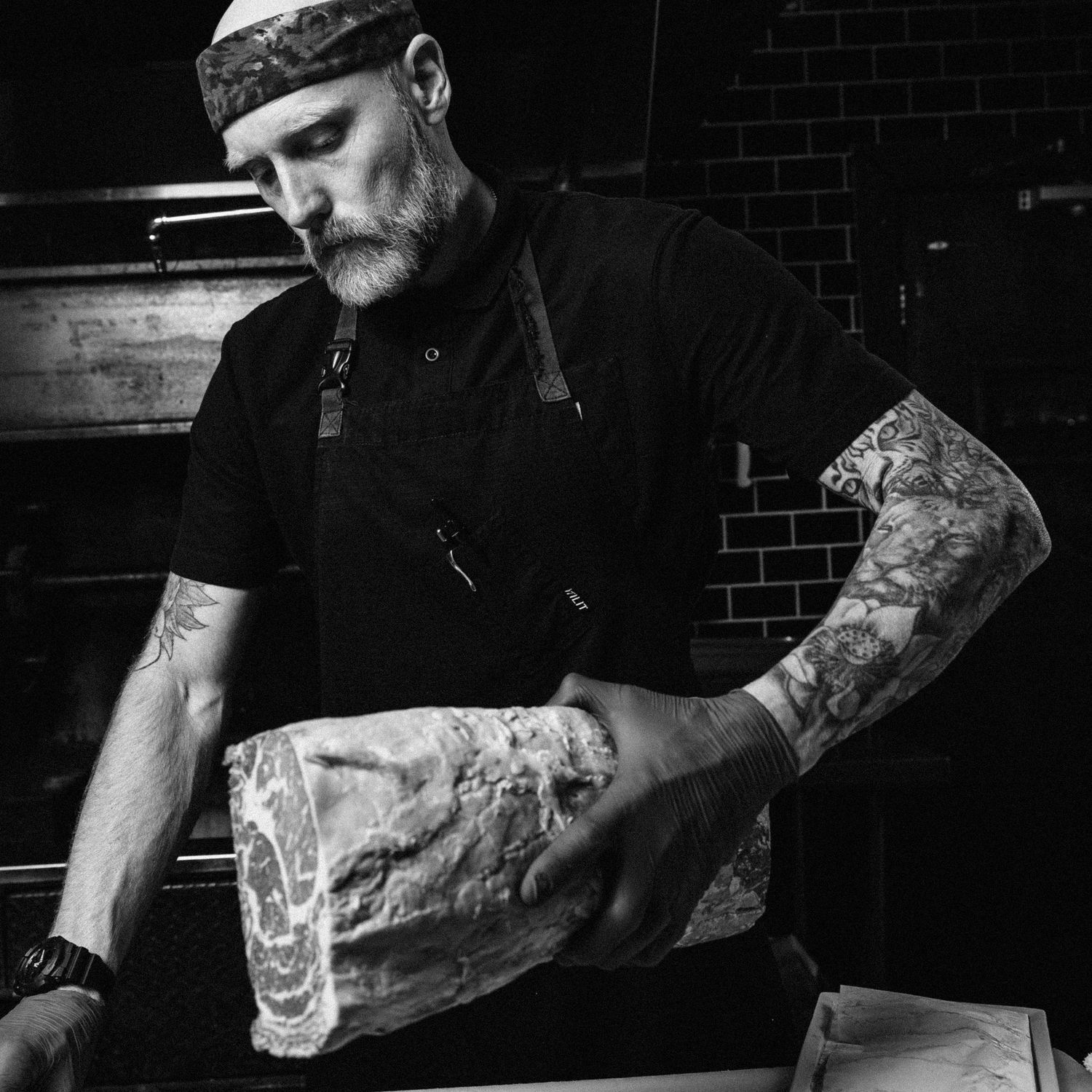 Professional butcher in black attire preparing meat on wooden cutting board.