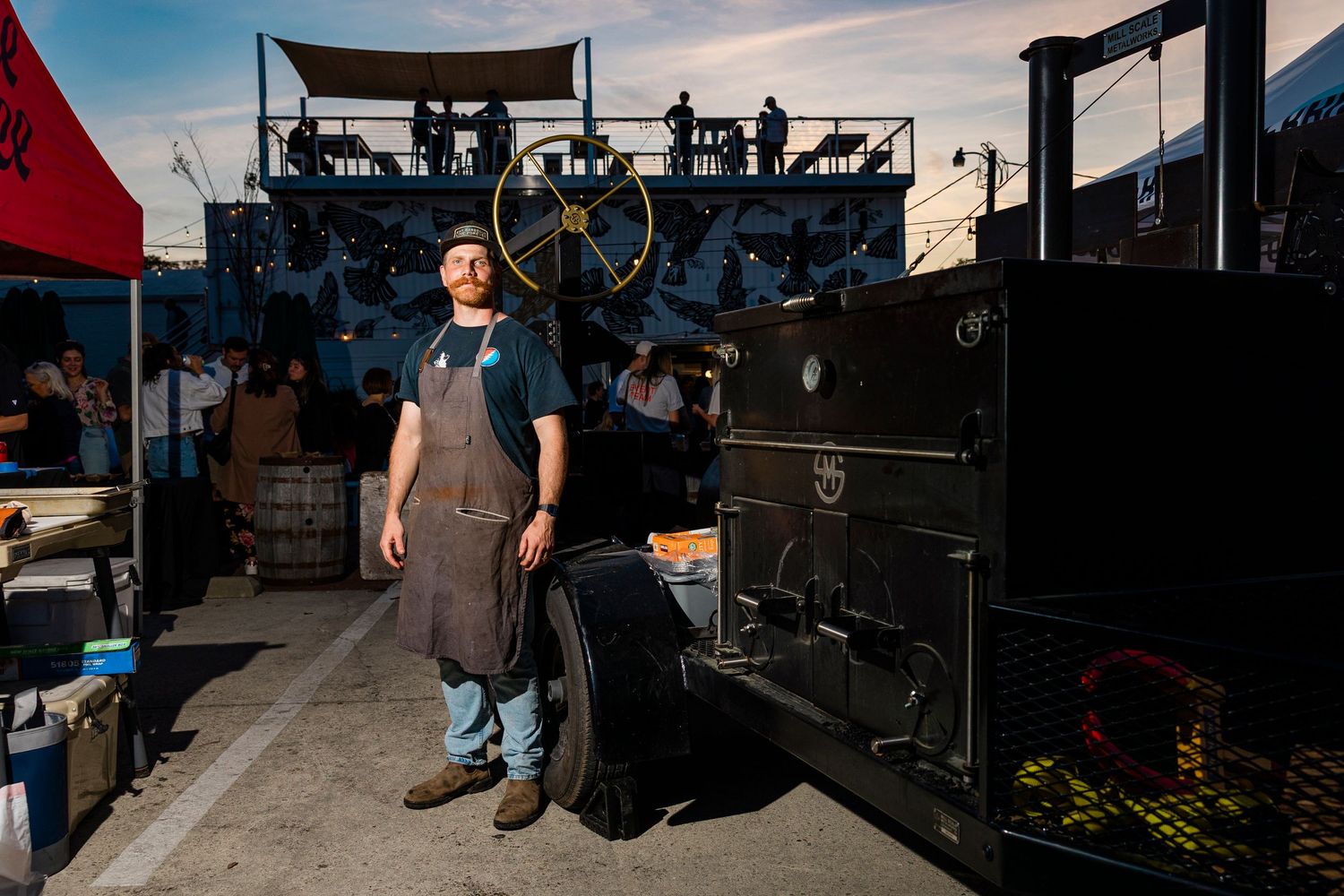 BBQ food trailer setup with smokers and outdoor cooking equipment under blue sky.