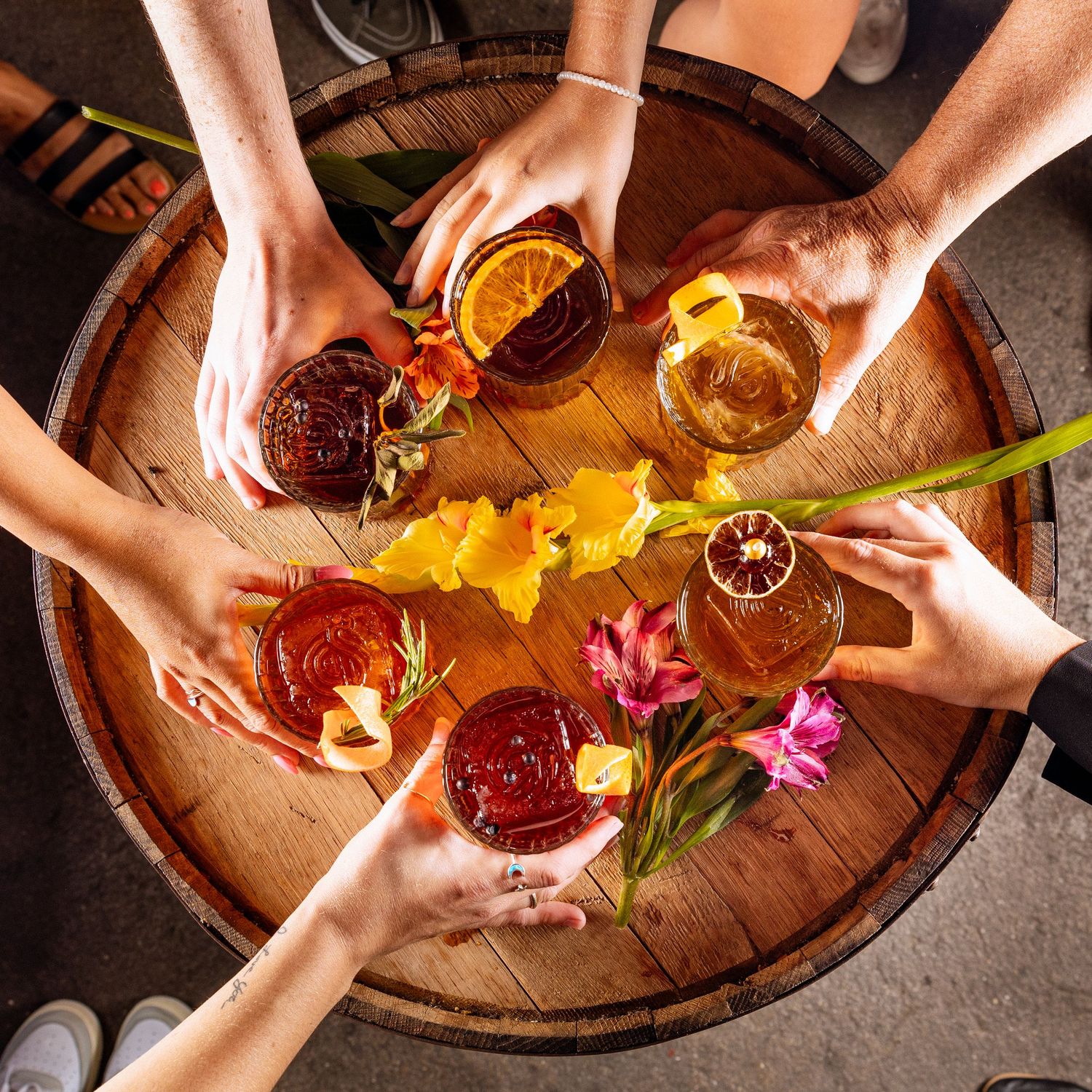 Overhead view of hands sharing colorful cocktails on wooden serving tray.