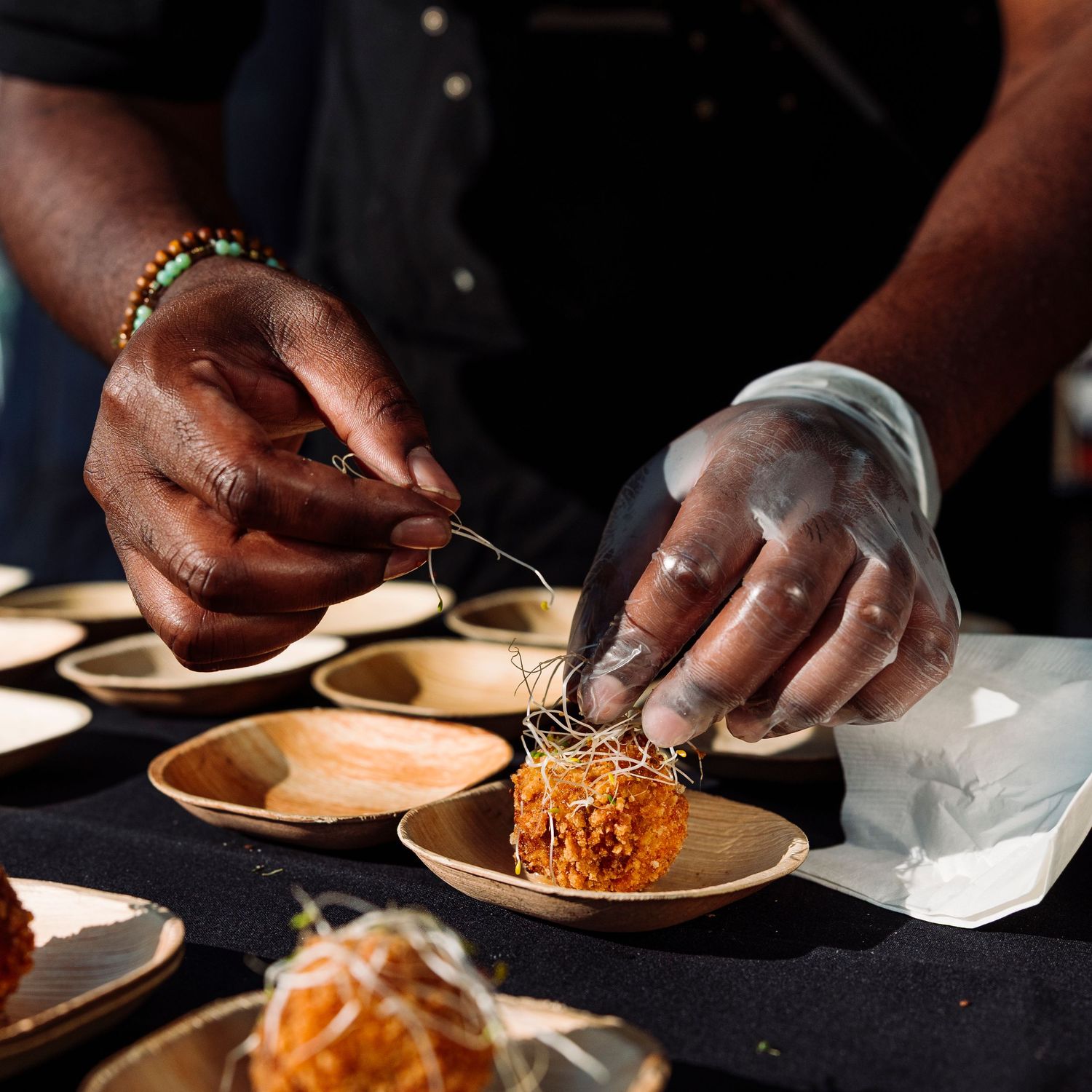 Hands plating food on wooden dishes at a culinary event.