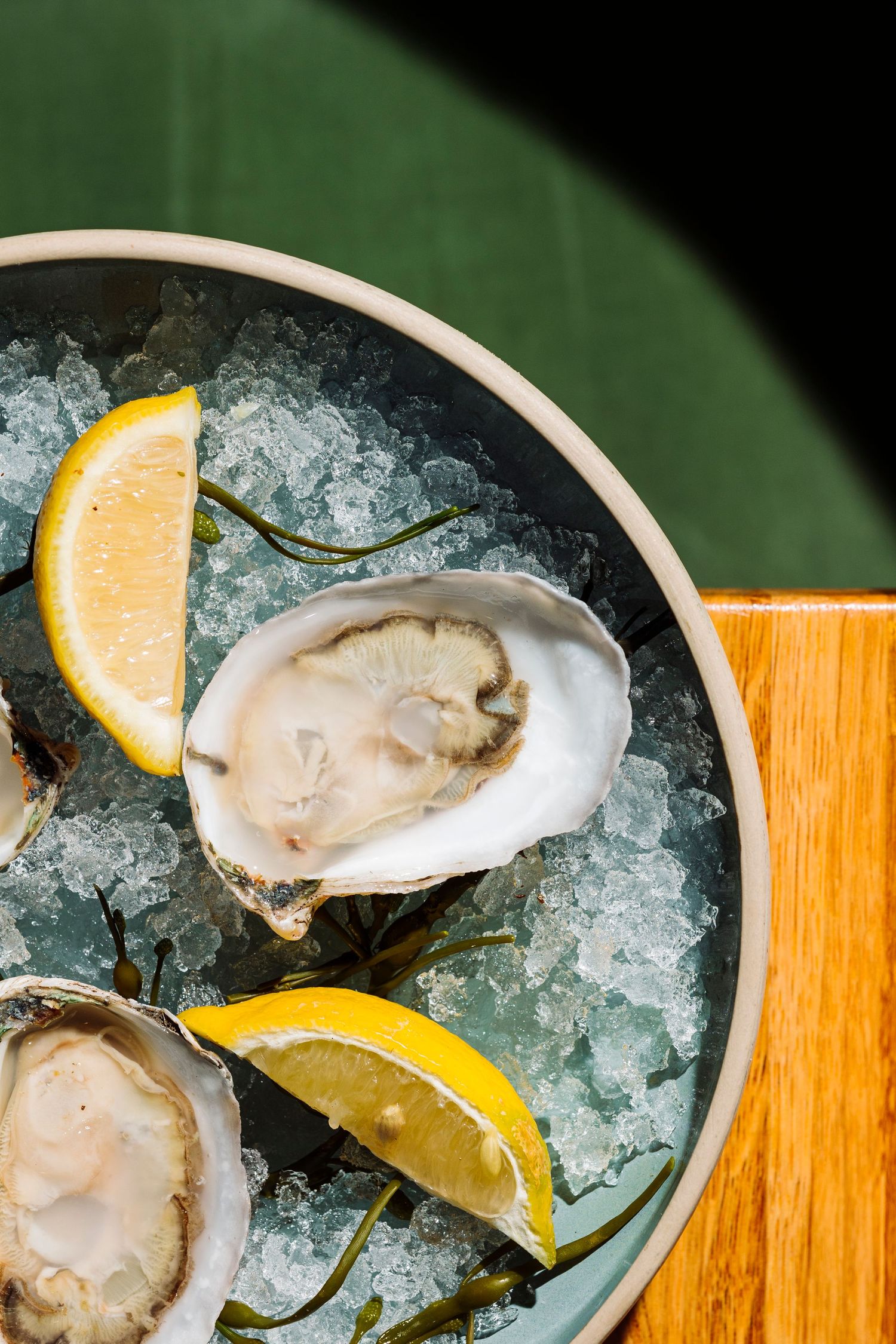 Fresh raw oysters on crushed ice with lemon wedges in white ceramic bowl.