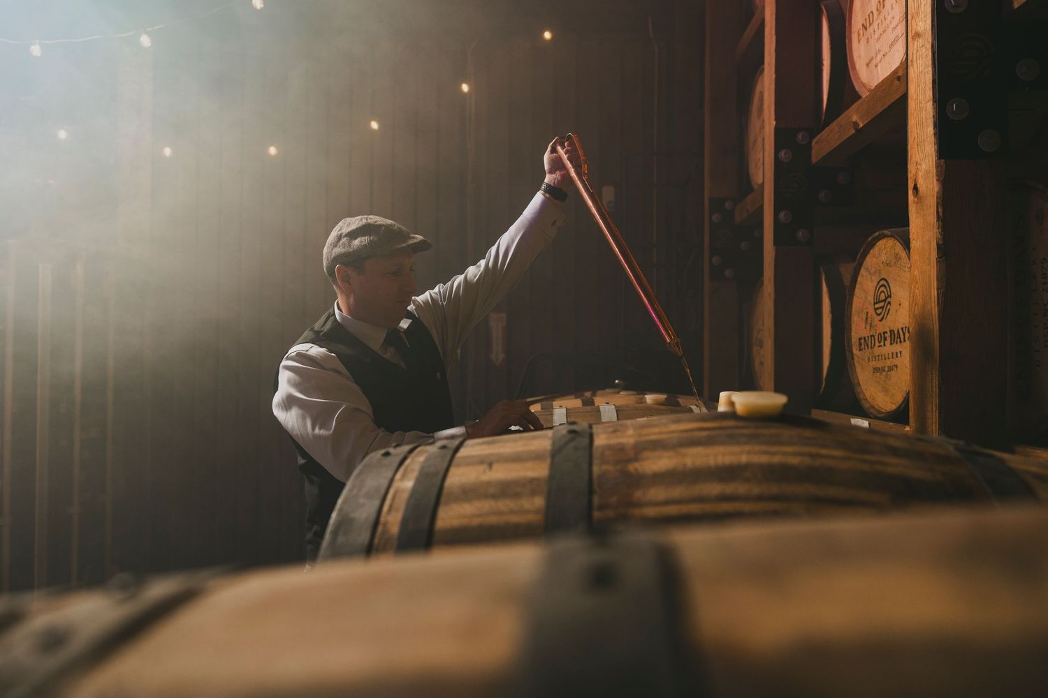 Person sampling wine from barrel in dimly lit cellar.