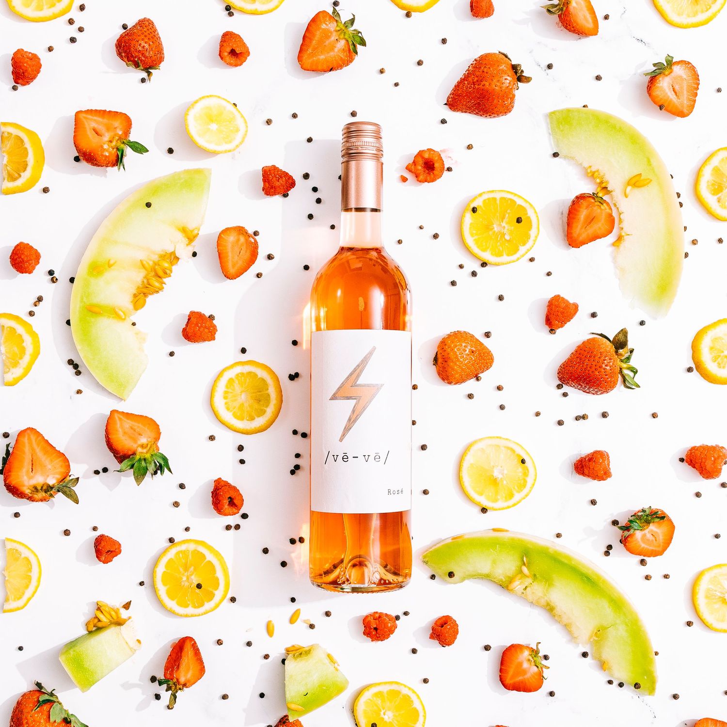 Flat lay of rose wine bottle surrounded by fresh strawberries and citrus slices on white background.