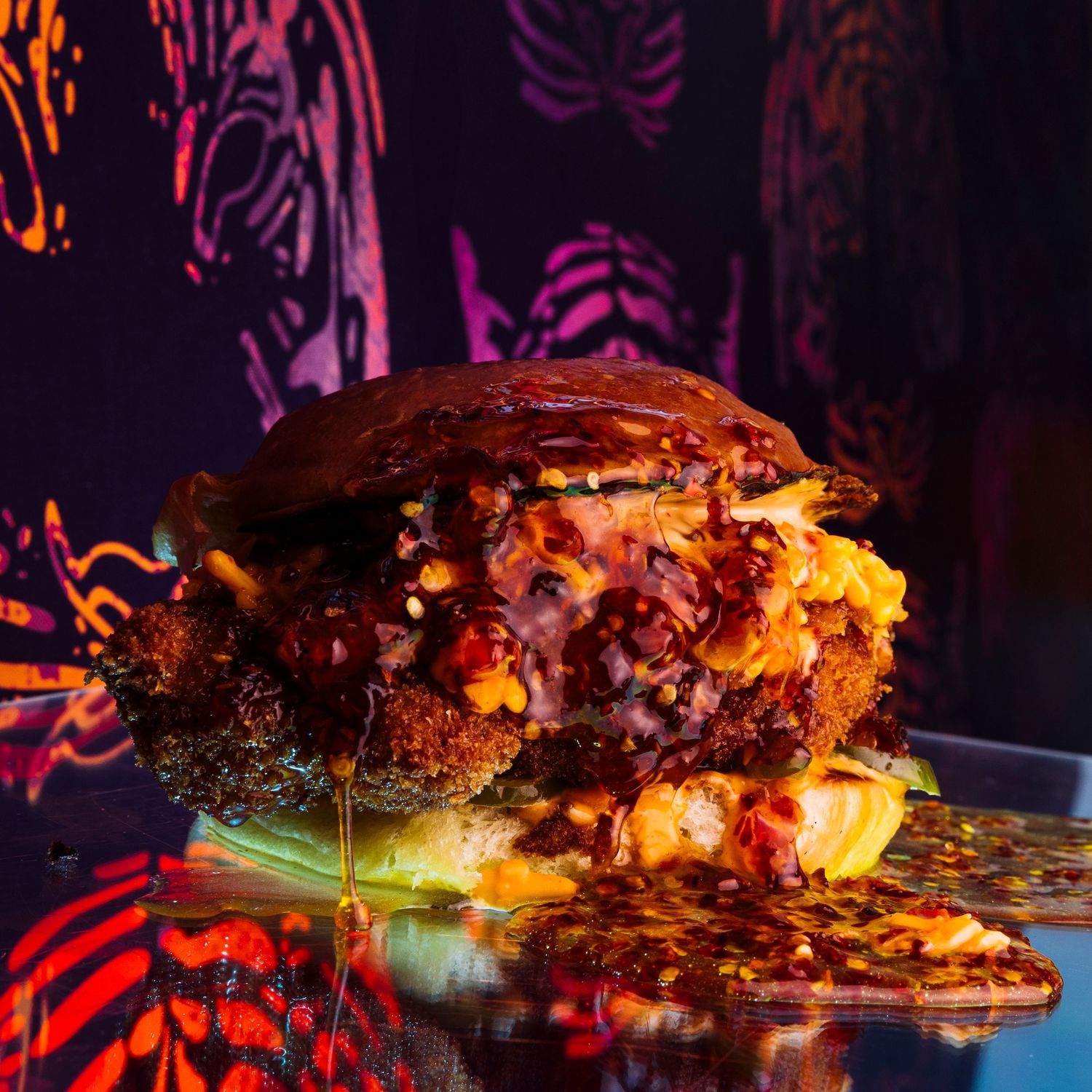 Gourmet burger with melted cheese and dripping sauce against a neon-lit background with vibrant patterns.