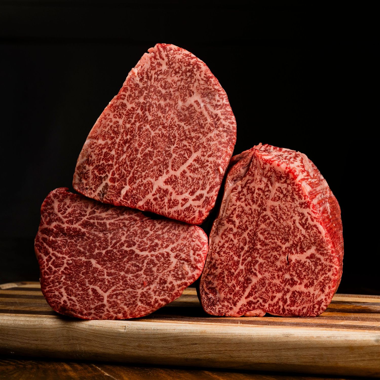 Marbled raw wagyu beef steaks against dark background showcasing intricate fat marbling patterns.