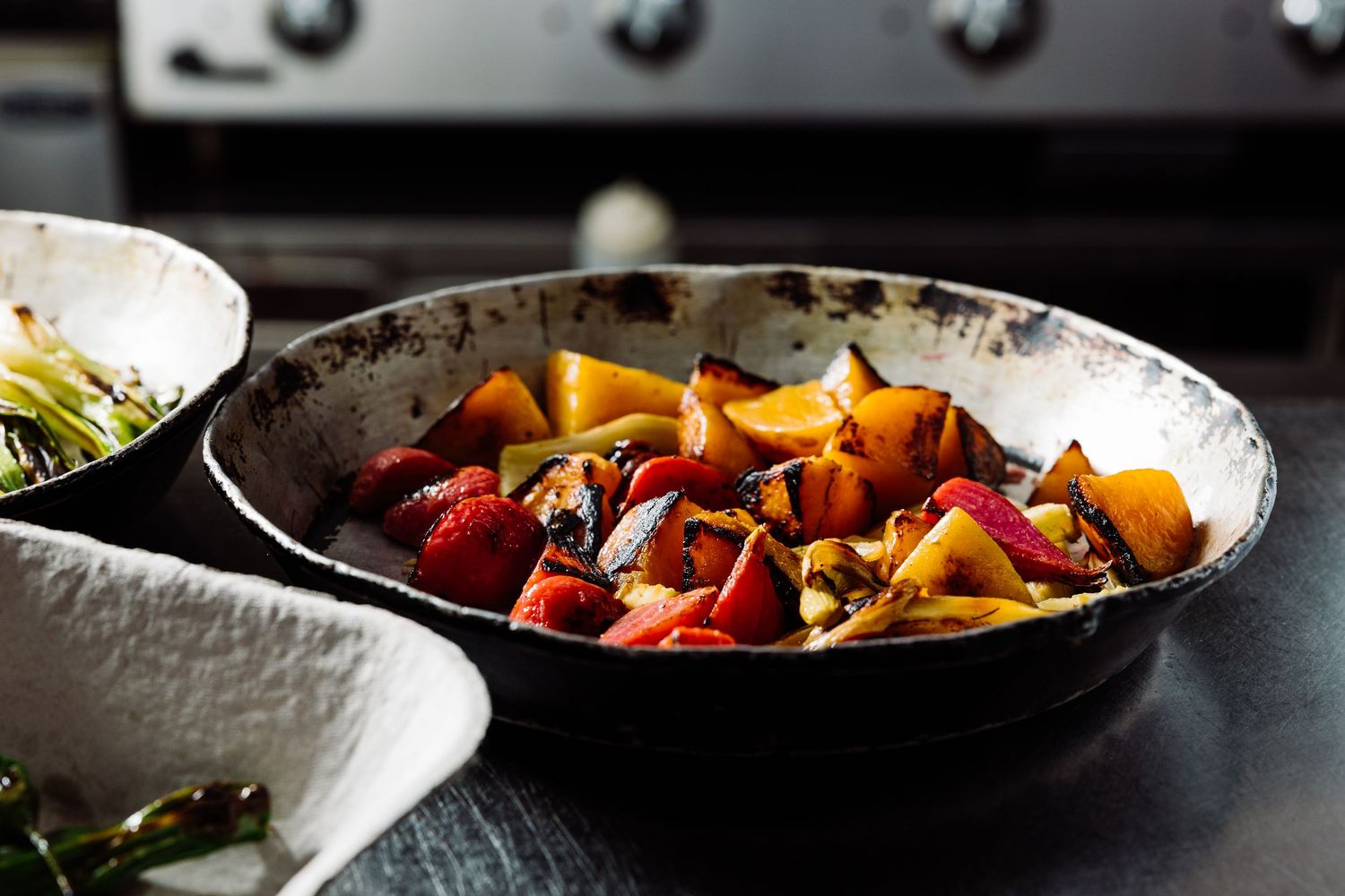 Series of cooking pans with fresh ingredients being prepared in dark moody lighting.
