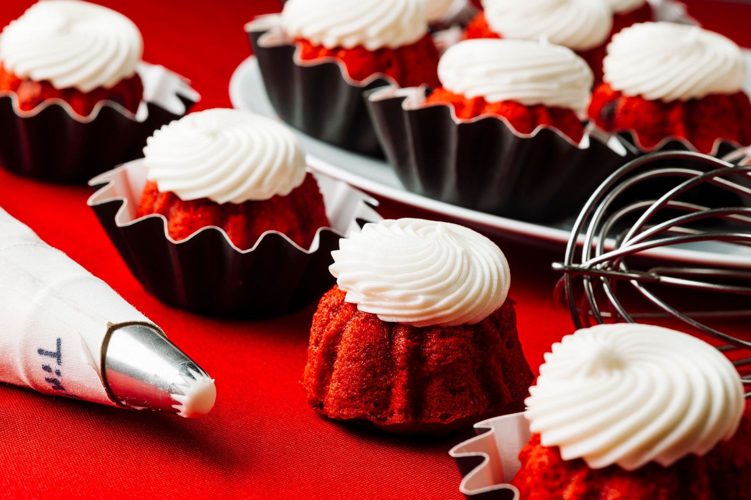 Red velvet cupcakes with white frosting swirls arranged in a line on a bright red background.