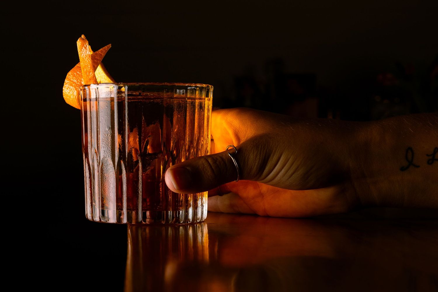 Amber-colored cocktail served in crystal glass with dramatic lighting and shadow.