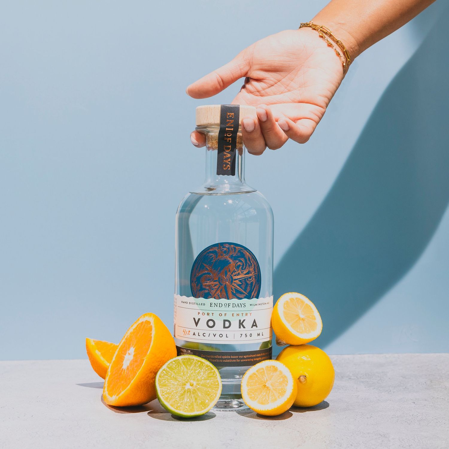 Bottle of craft vodka with fresh citrus fruits arranged on light blue background.