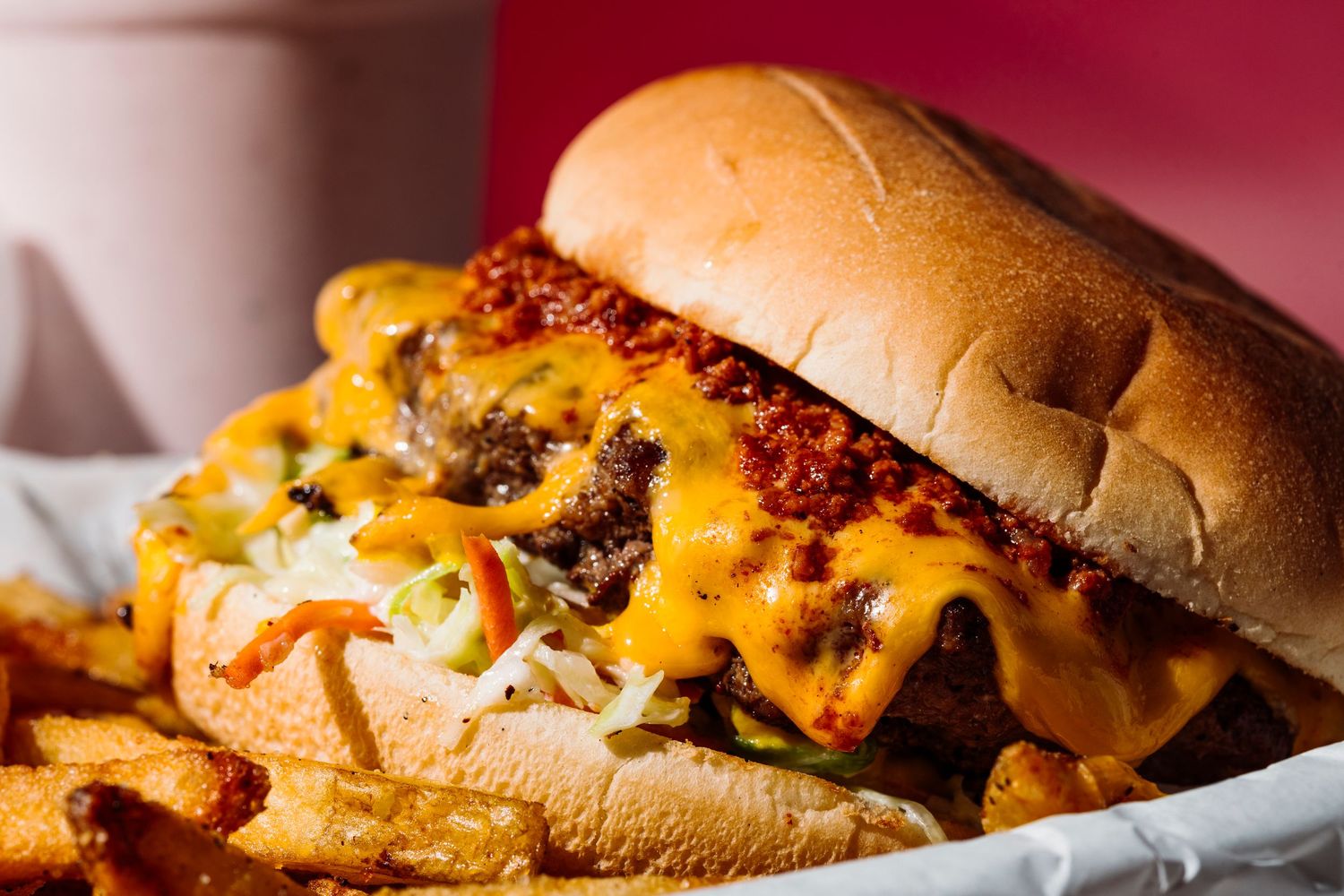 Close-up of cheeseburger with melted cheese and fries on white paper.
