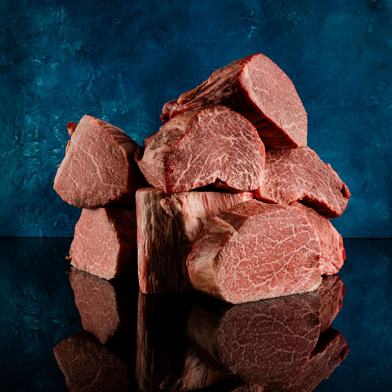 Premium cut raw beef steaks arranged on dark blue surface with reflection.