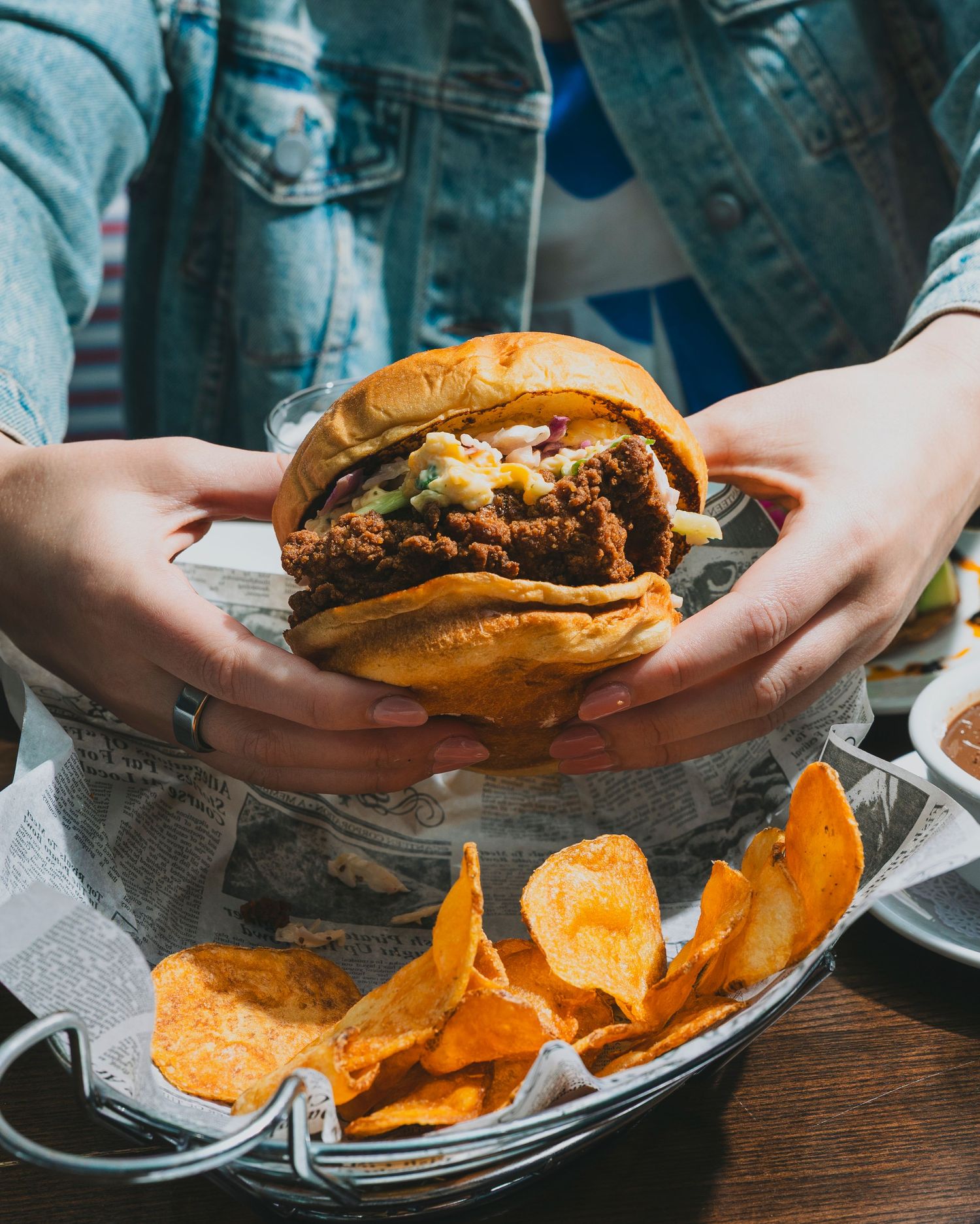 Multiple hamburgers with cheese and toppings served with crispy potato chips on wooden plates.