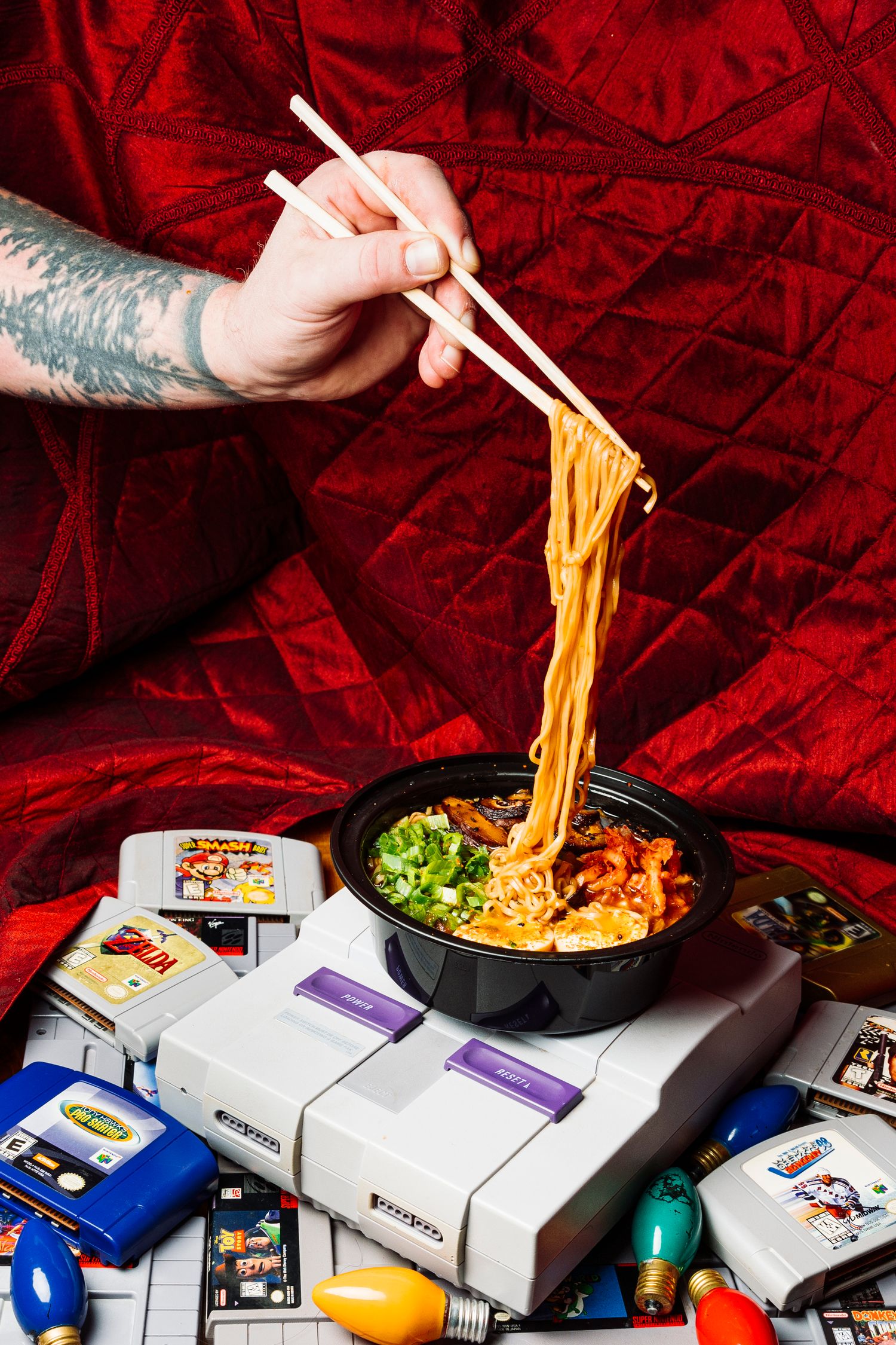 Chopsticks lifting ramen noodles from a bowl placed on top of a retro gaming console with cartridges.
