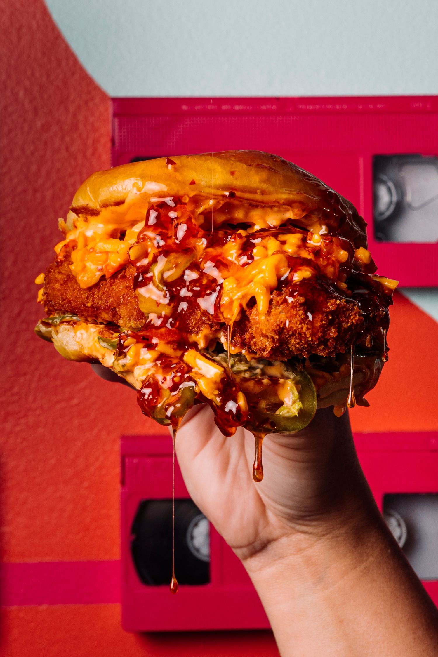 Juicy cheeseburger with melting sauce held up against a red background.