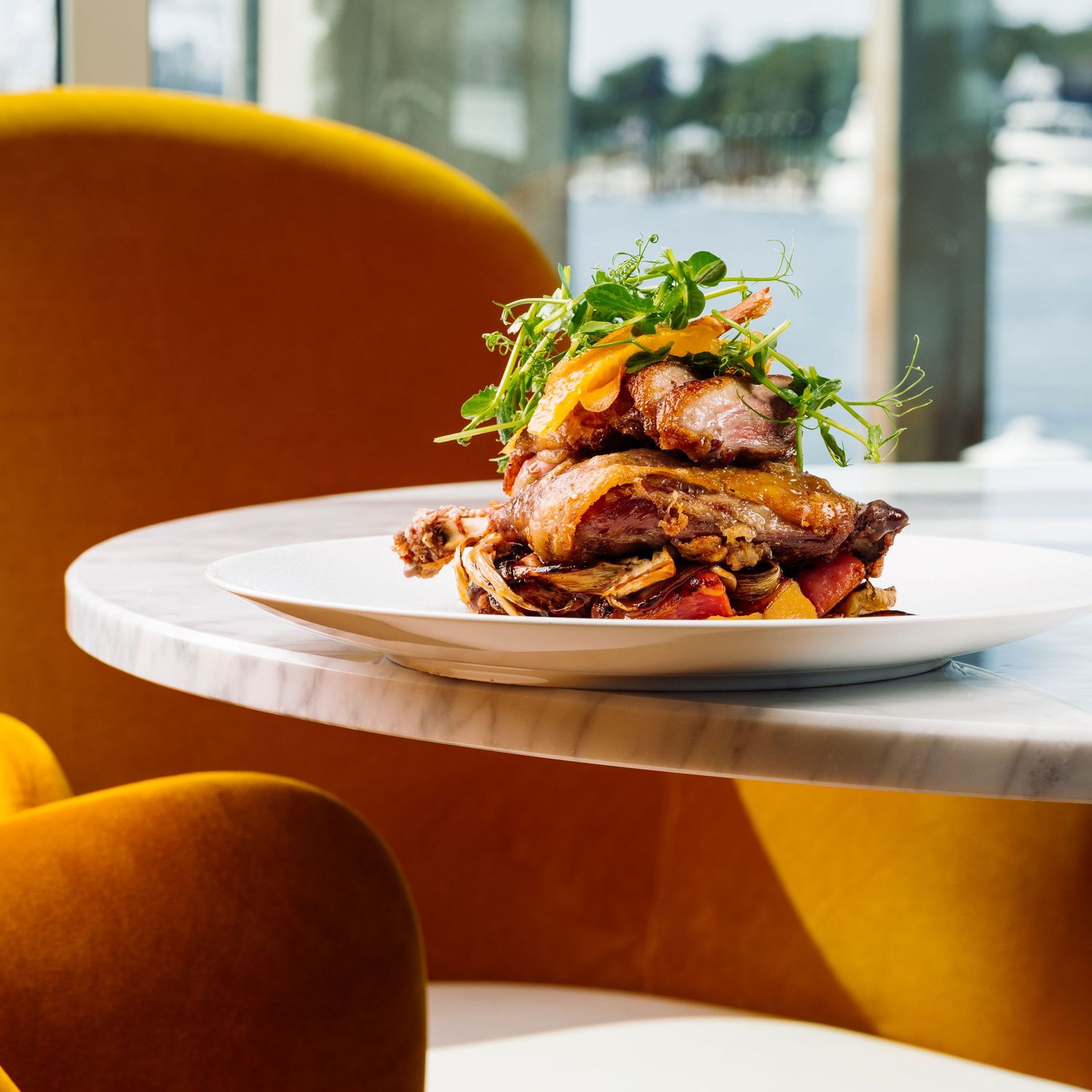 Beautifully plated meat dish with garnish served on white plates in restaurant setting.