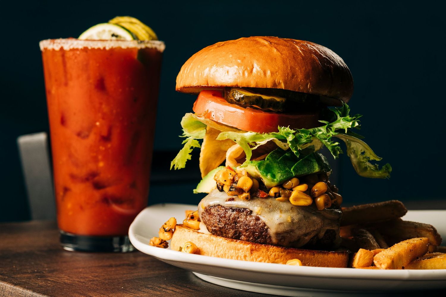 Gourmet burger lineup and cocktails against a dark background with dramatic side lighting.