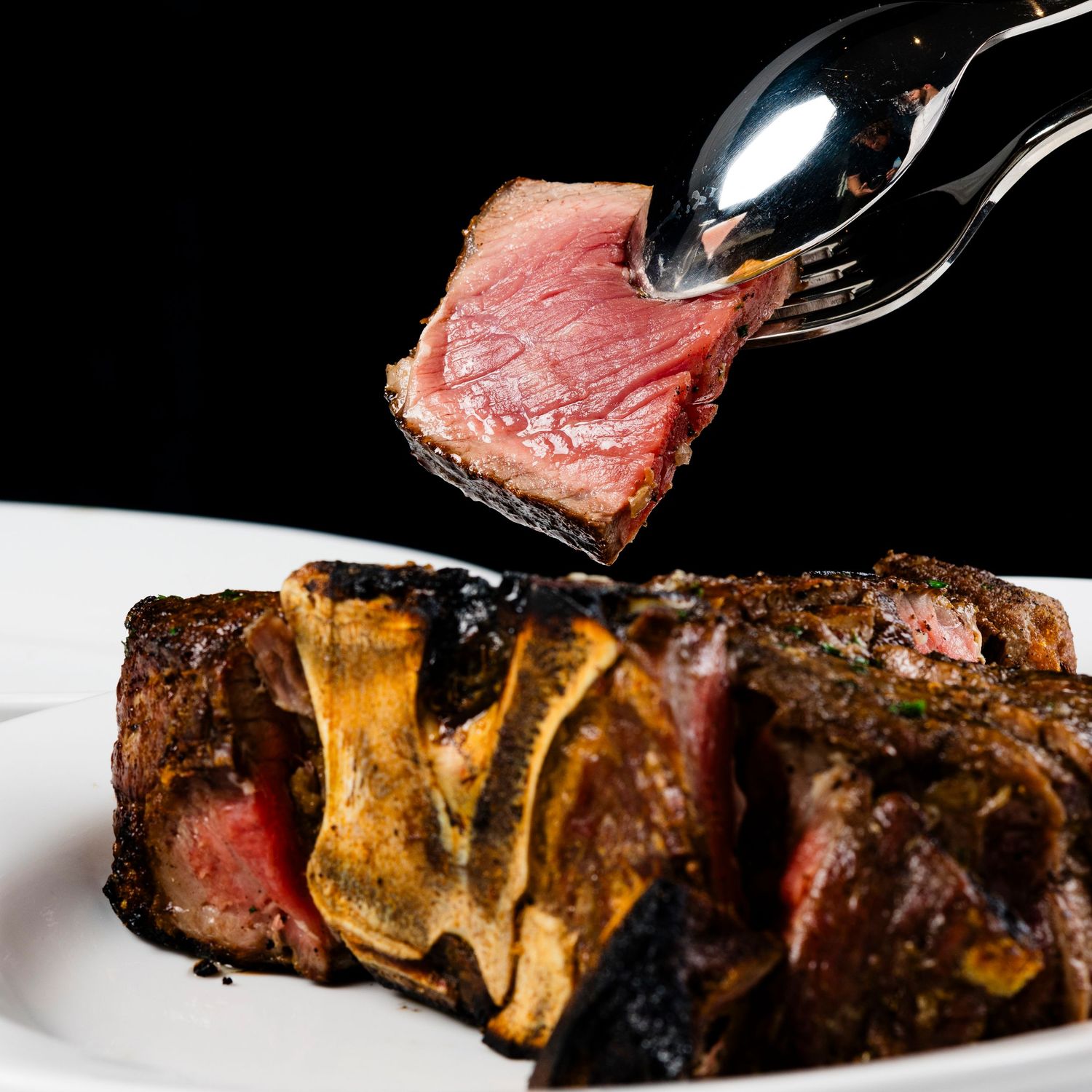 Slicing medium-rare steak showing juicy pink center against dark background.
