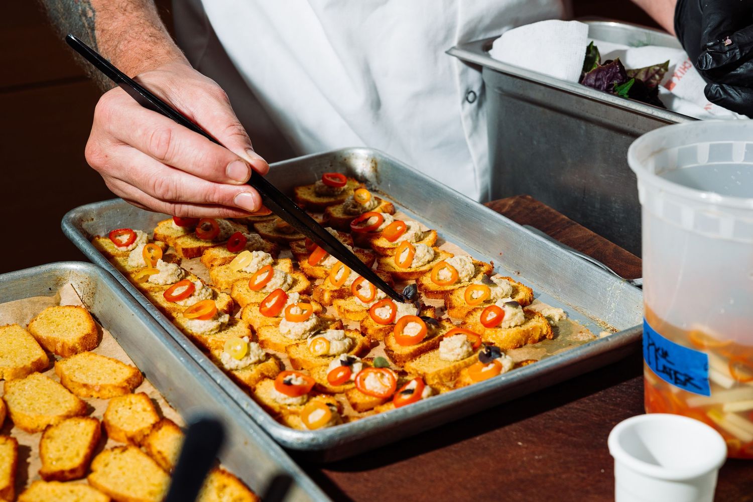 Sheet pans of roasted shrimp being seasoned and prepared in a commercial kitchen.