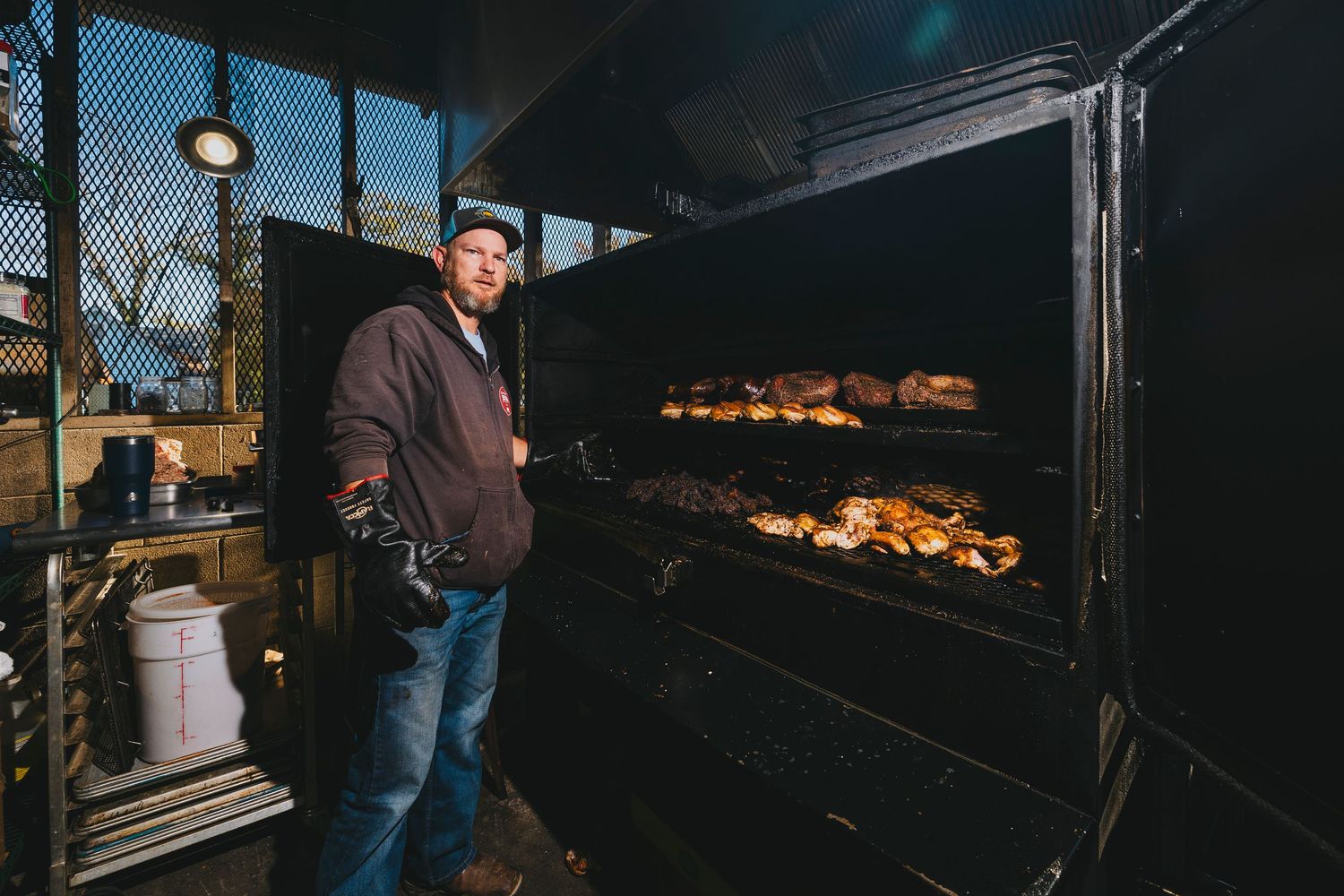 Large commercial smoker with glowing coals and meat cooking inside.