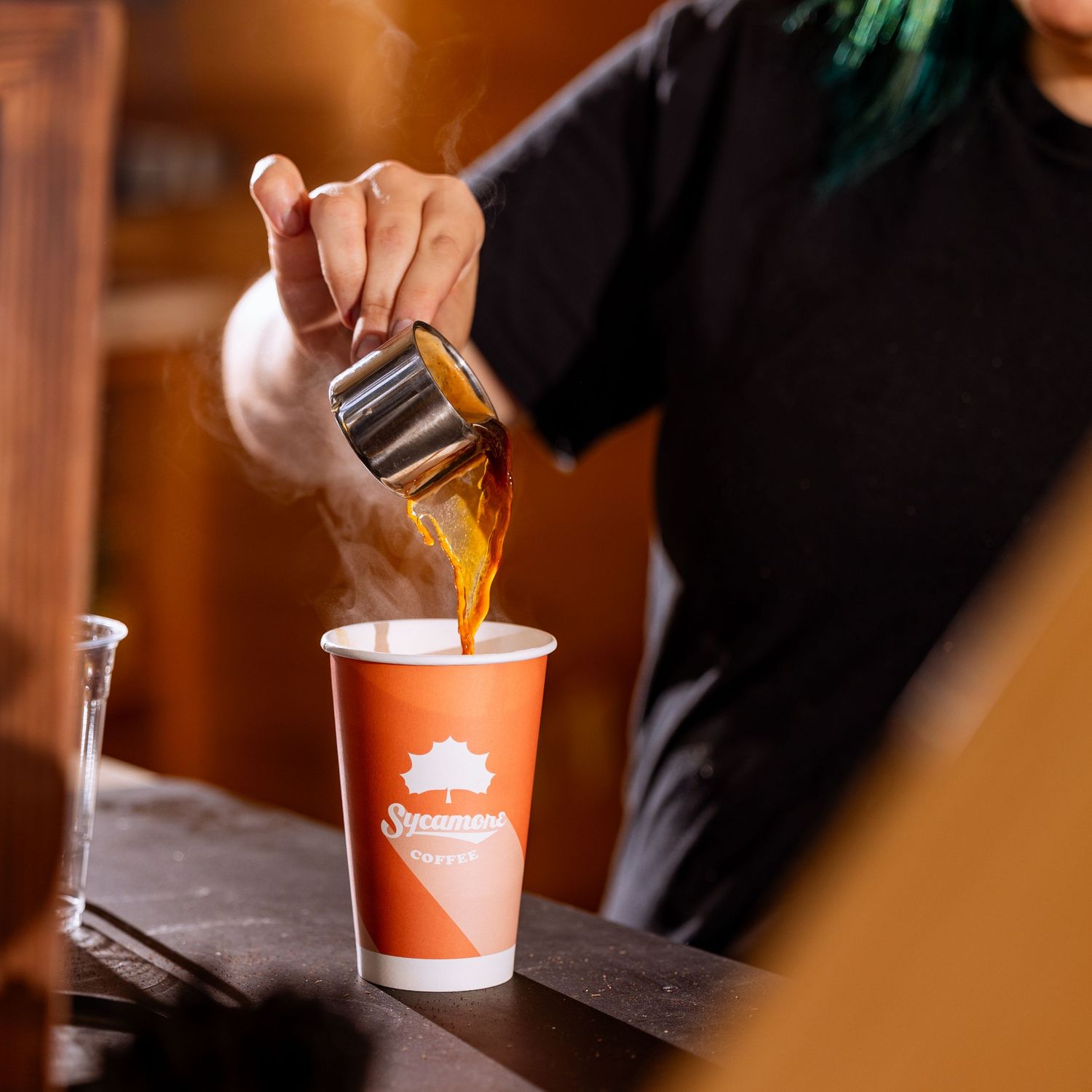 Metal shaker pouring espresso into small red disposable cups.