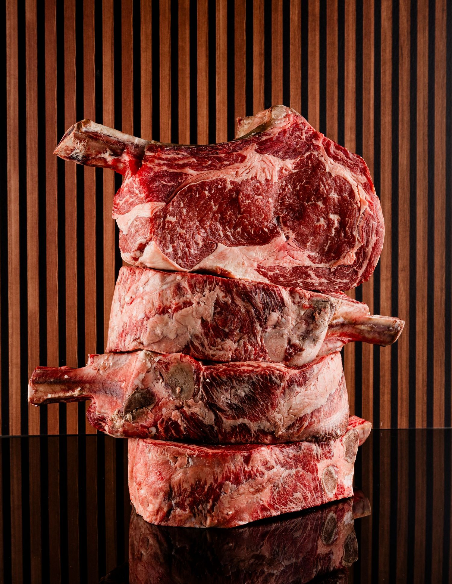 Stack of raw ribeye steaks against wooden slat background.