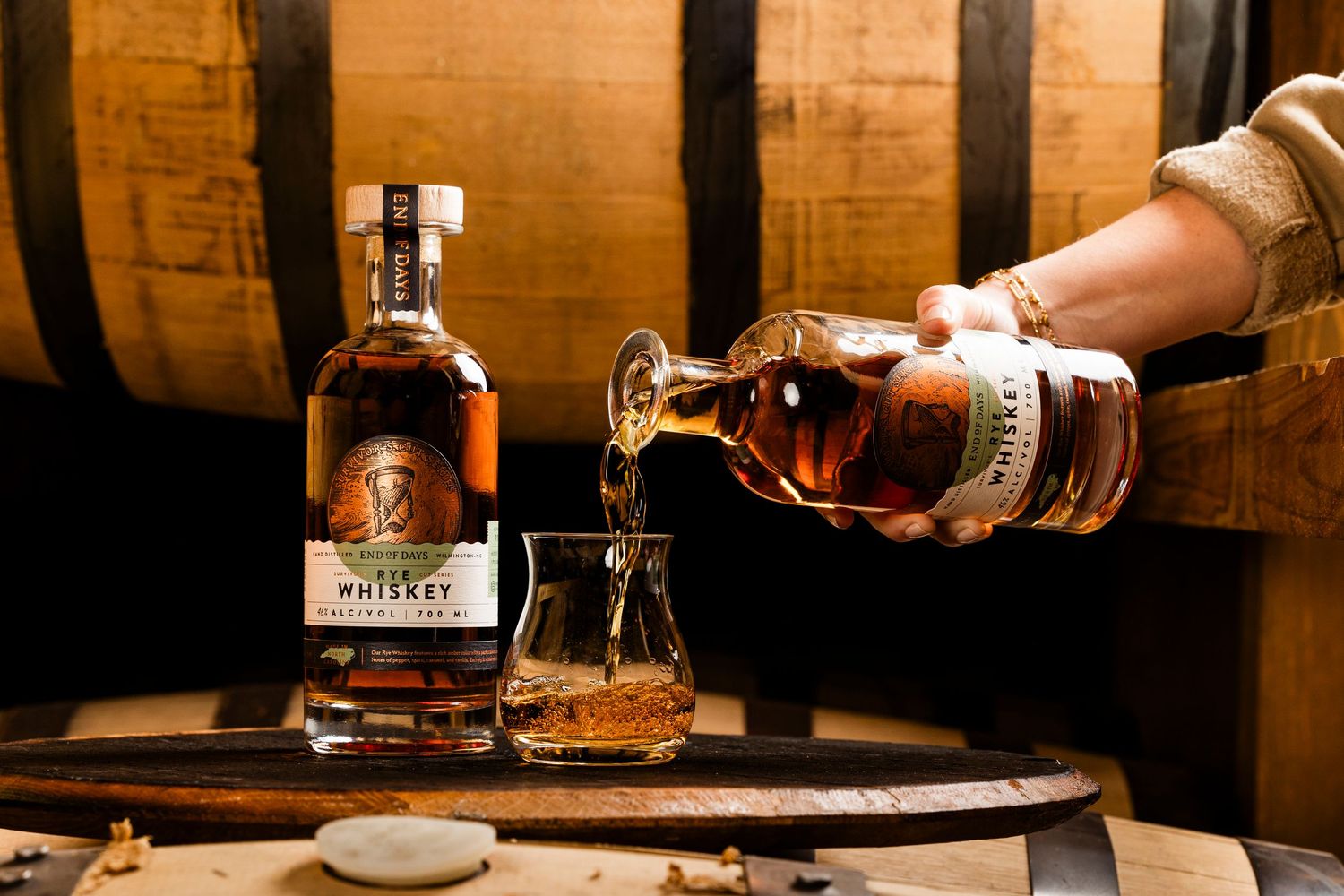 Wooden barrels in a dimly lit cellar with hands pouring spirits into glasses.