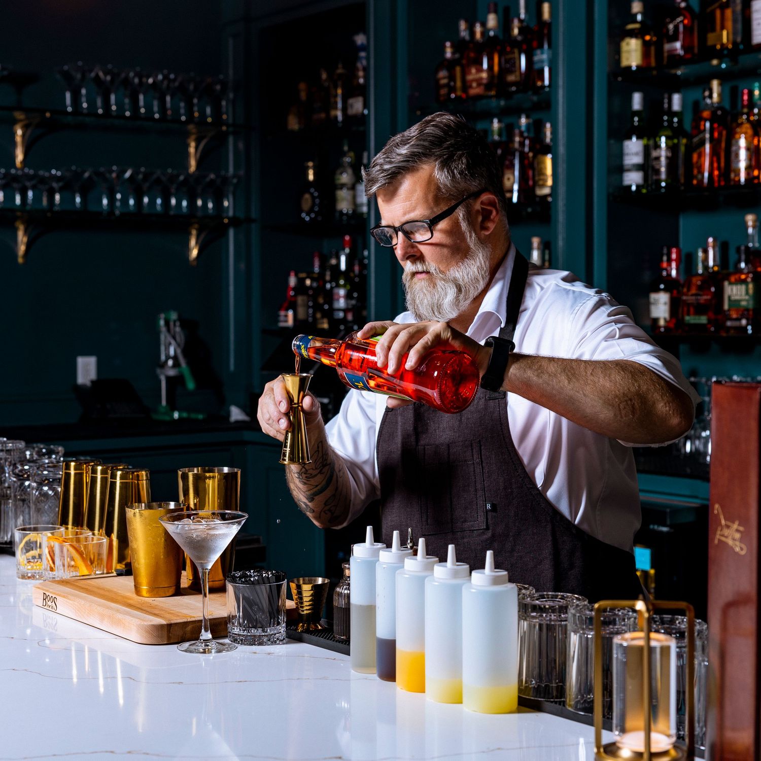 Bartender pouring and mixing colorful cocktails at an upscale bar counter.