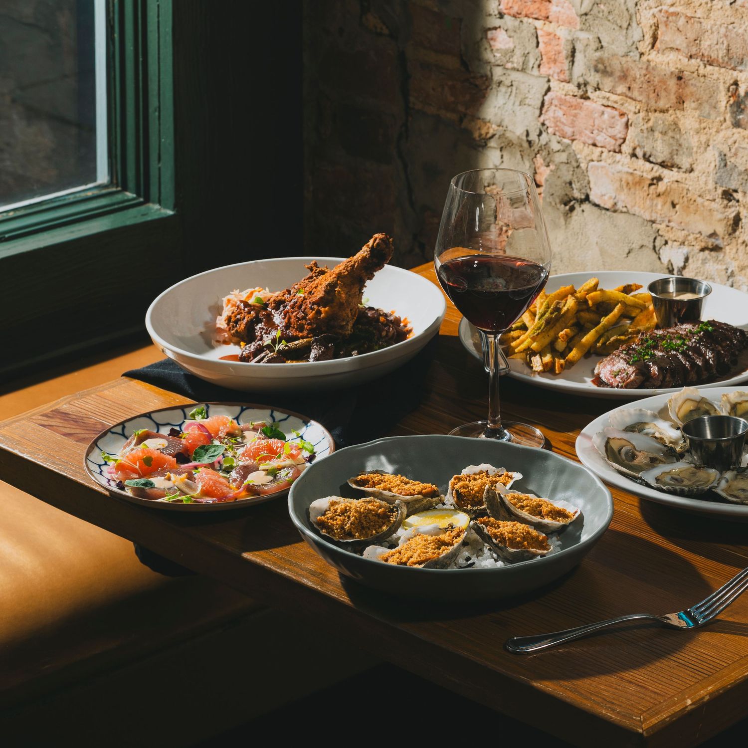 Rustic plated dishes on a wooden table in dramatic lighting with exposed brick wall background.