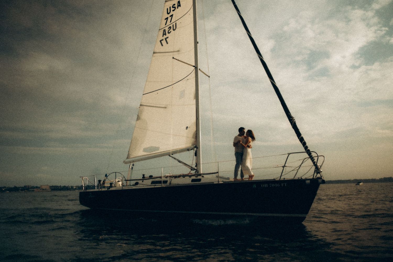 Couple embracing on a sailboat at sea under a dramatic cloudy sky at dusk.