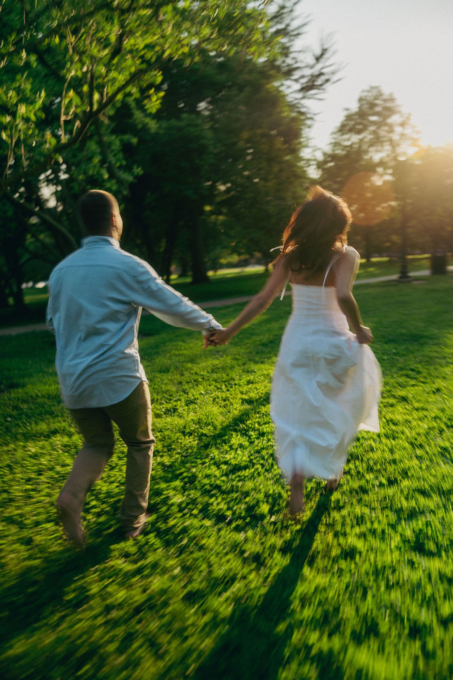 Playful couple running through green field at sunset.