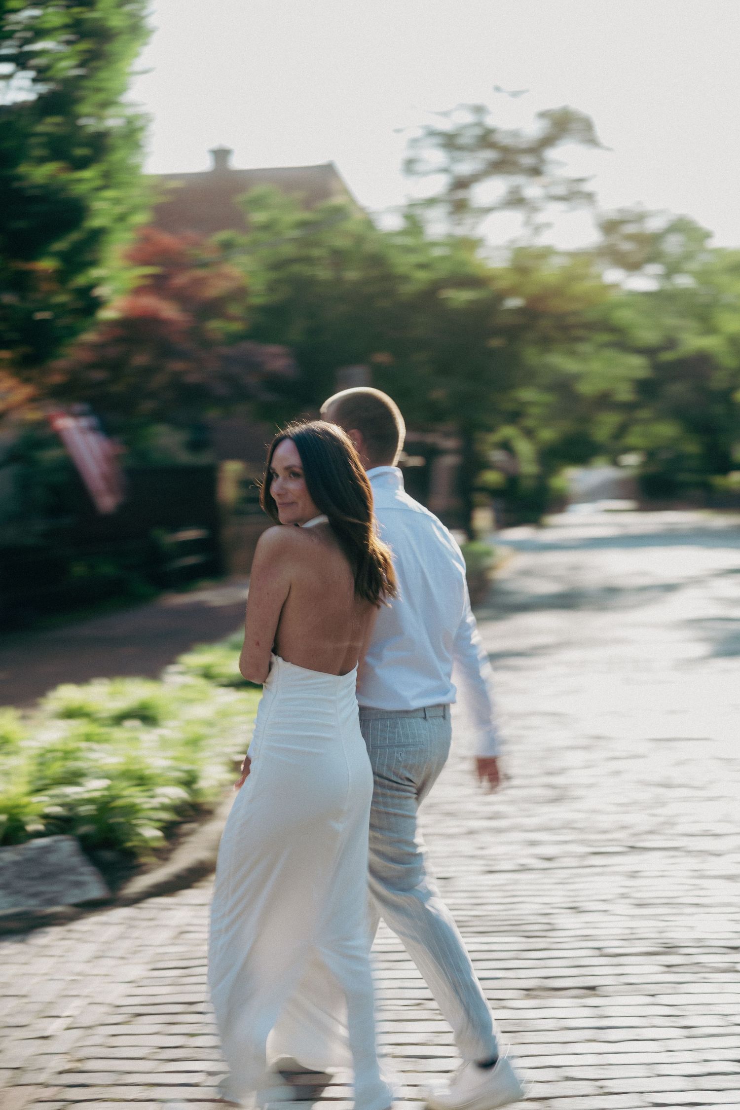 A couple in white clothing dances together on a cobblestone street in romantic sunlight.
