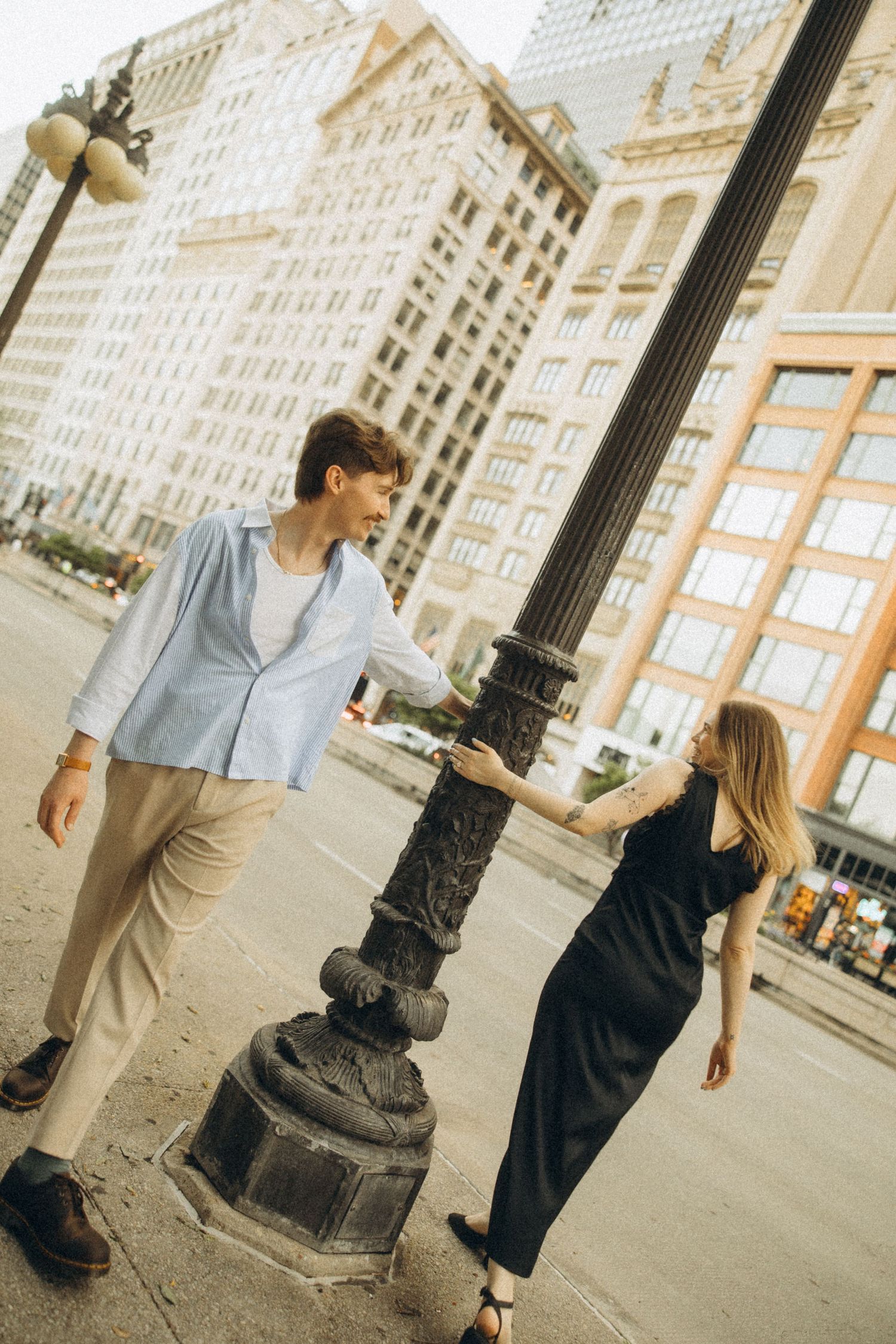 Two people standing near an ornate lamppost in an urban setting.
