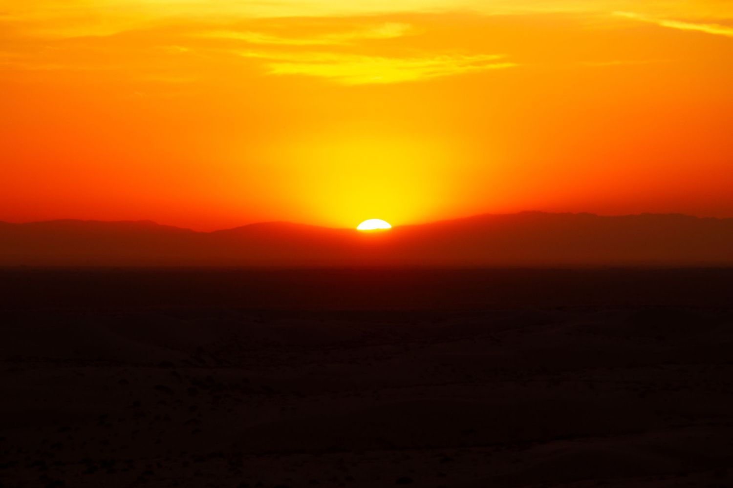 Dramatic orange sunset over mountain silhouettes creates a vibrant skyline.