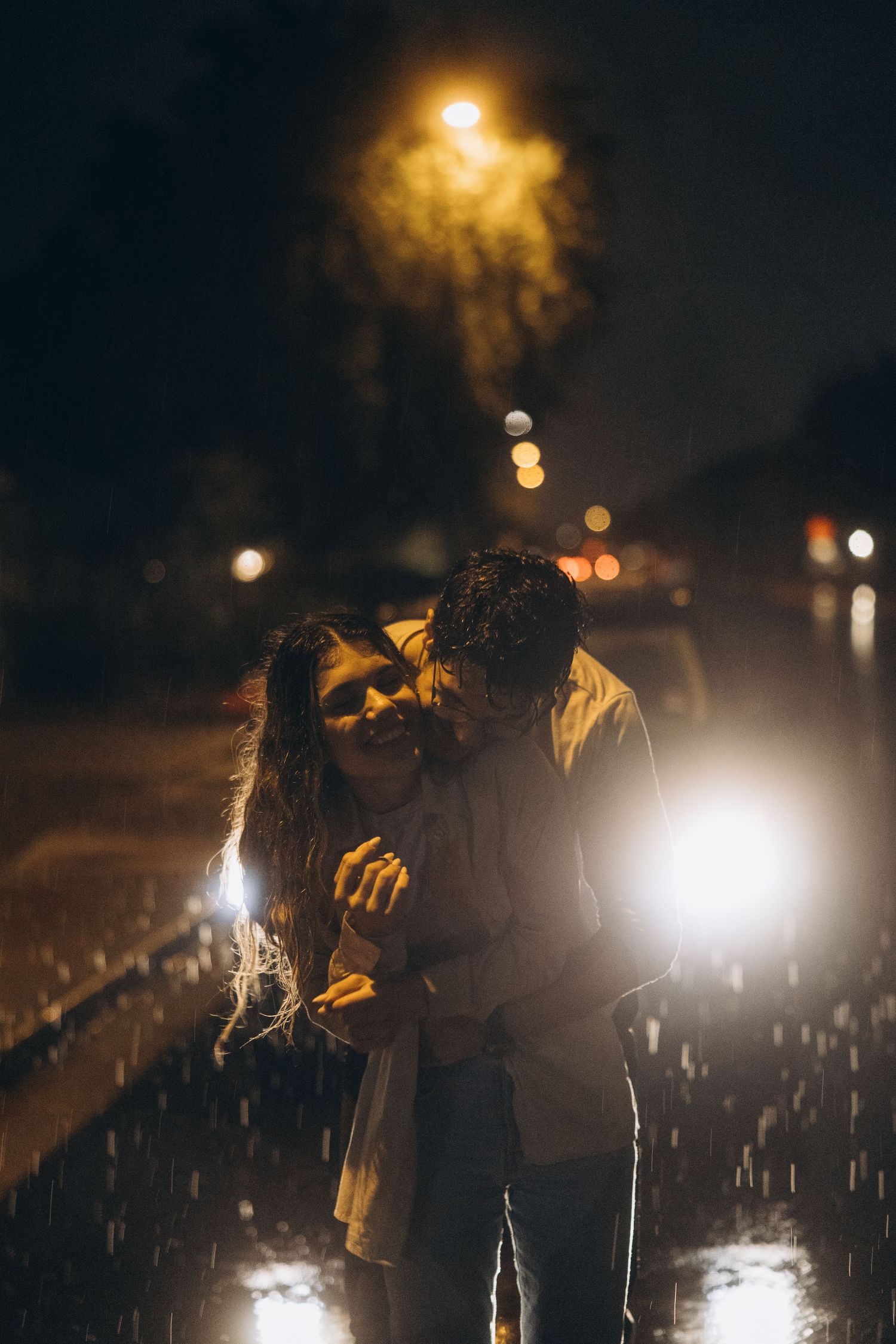 A romantic nighttime scene in the rain with bokeh lights and street lamps creating a moody atmosphere.