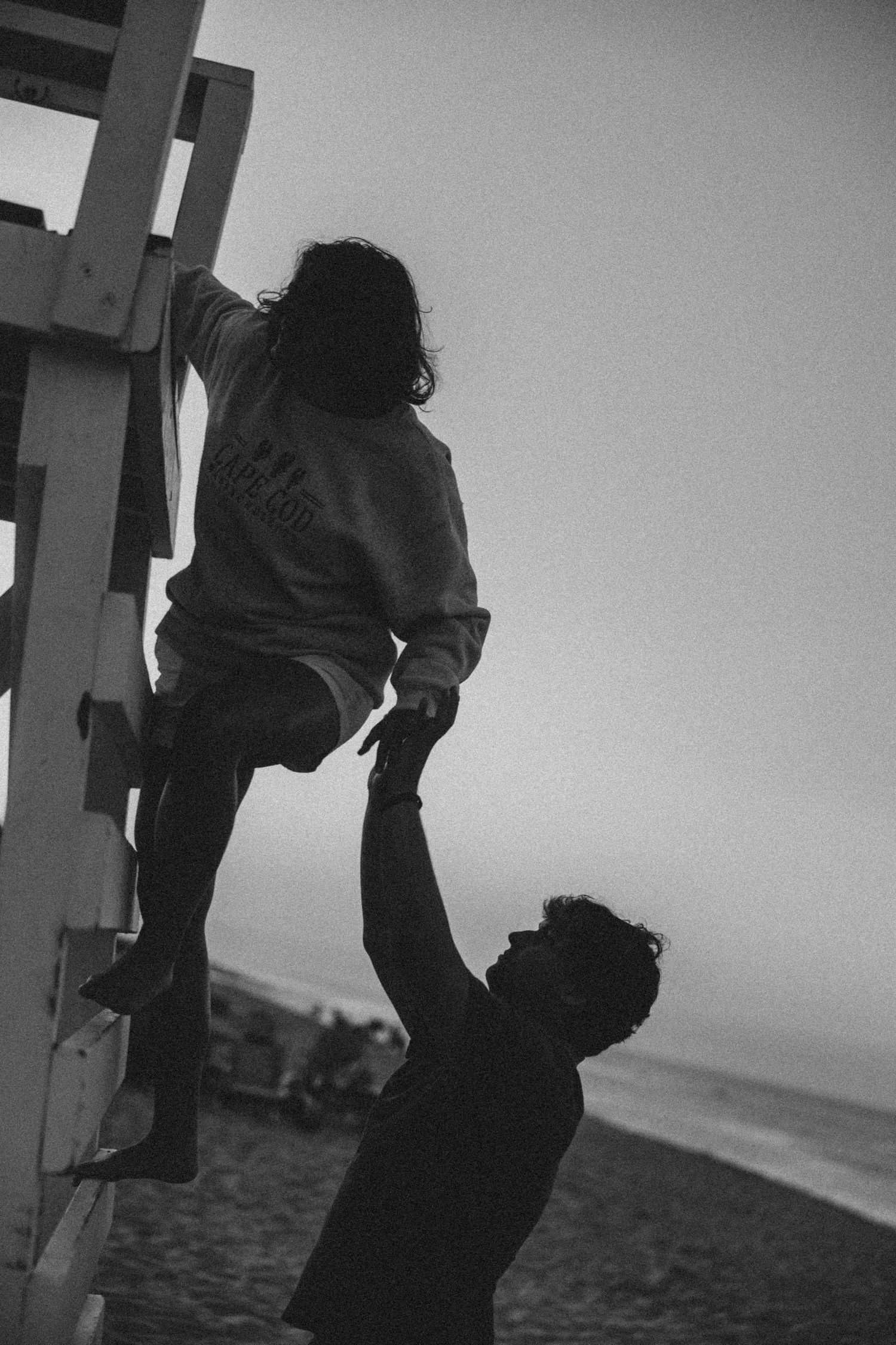 Black and white silhouettes of figures on a beach structure at dusk.