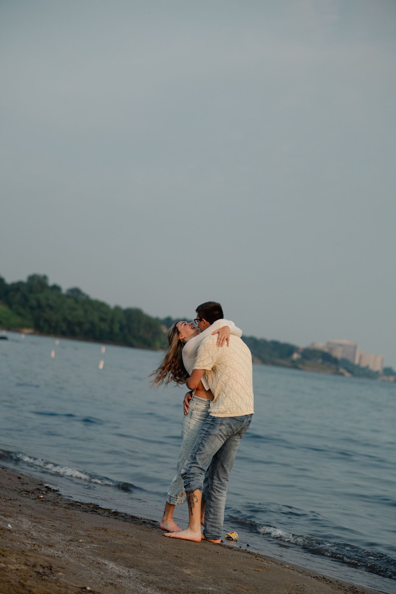 People enjoying a playful moment at the water's edge with city views in background.