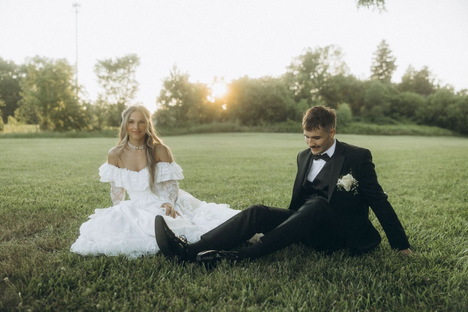 Wedding couple sitting together on grass during golden hour.