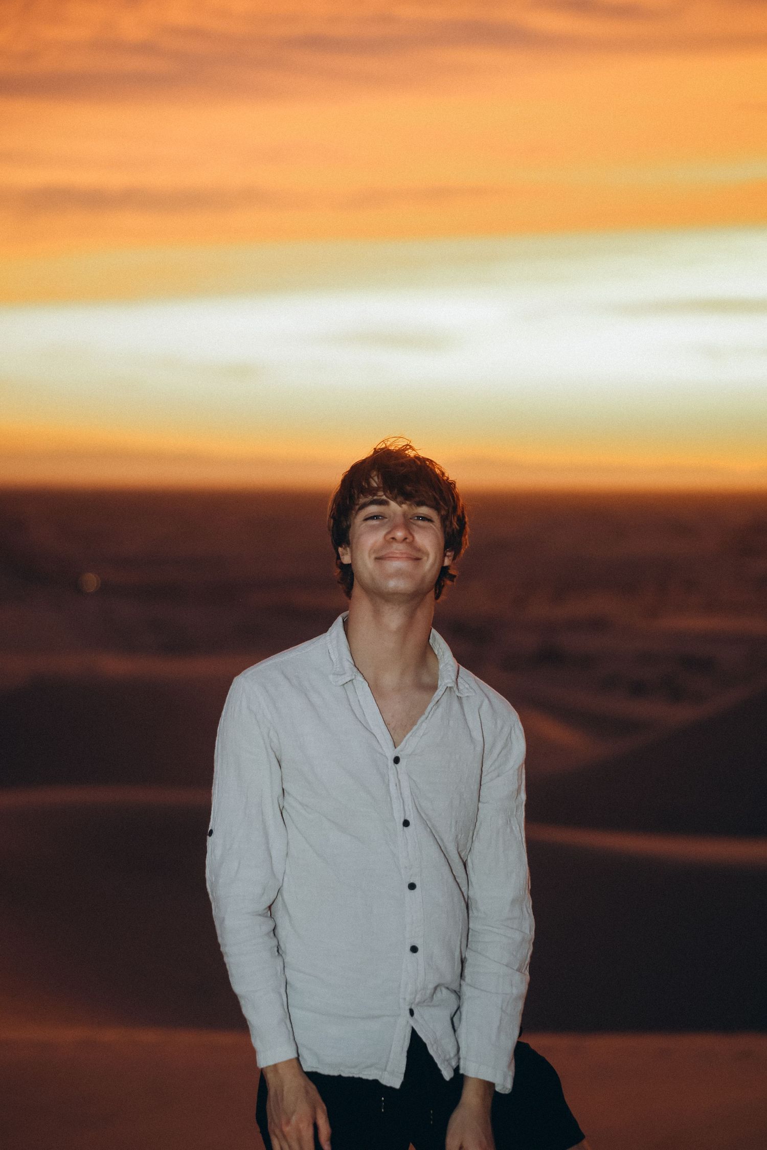 A person in white clothing poses against a dramatic orange sunset sky.