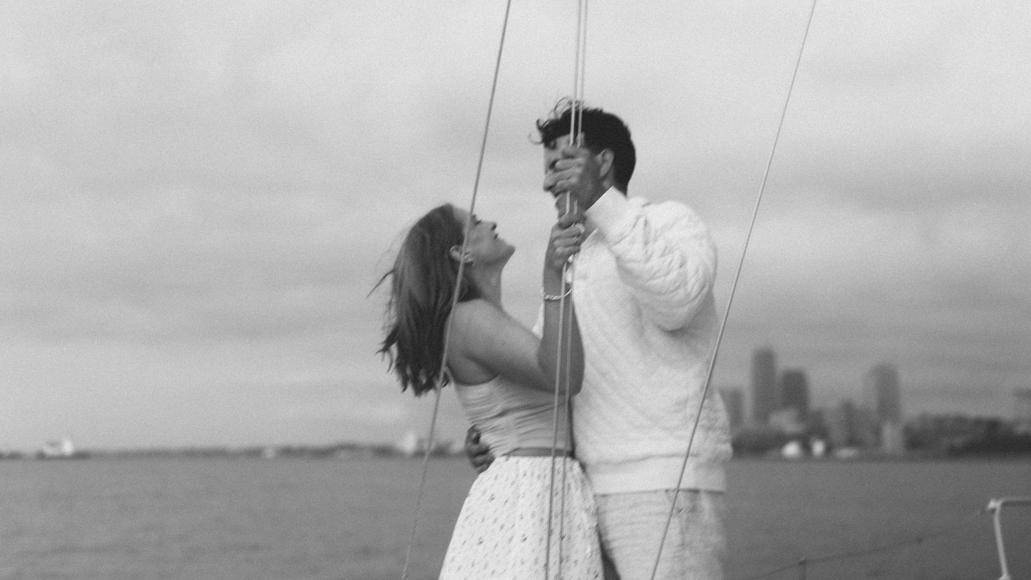 A couple shares a romantic kiss on their wedding day with a scenic waterfront backdrop.