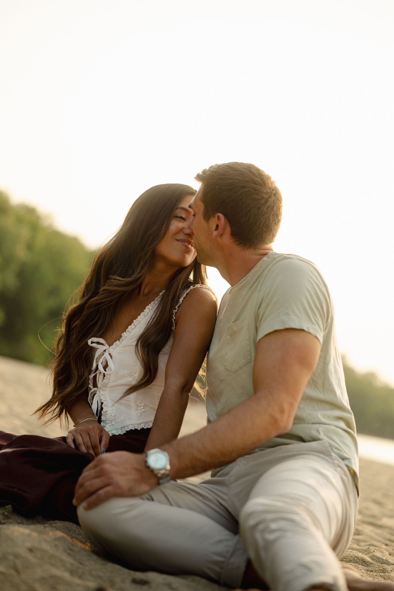 Intimate couple sharing tender moments on the beach during golden hour.