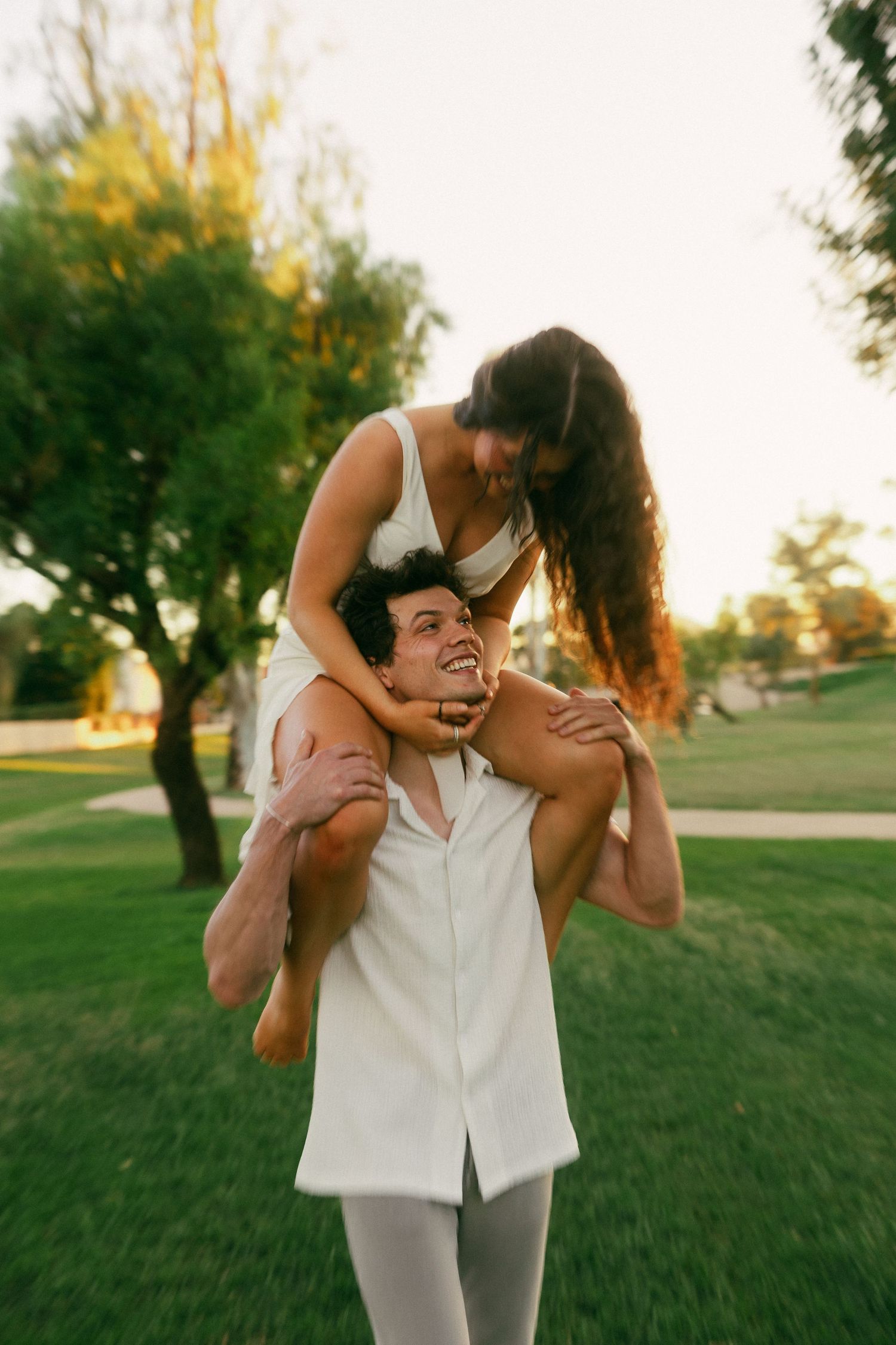 A playful couple enjoys a piggyback ride in a sunny park during golden hour.