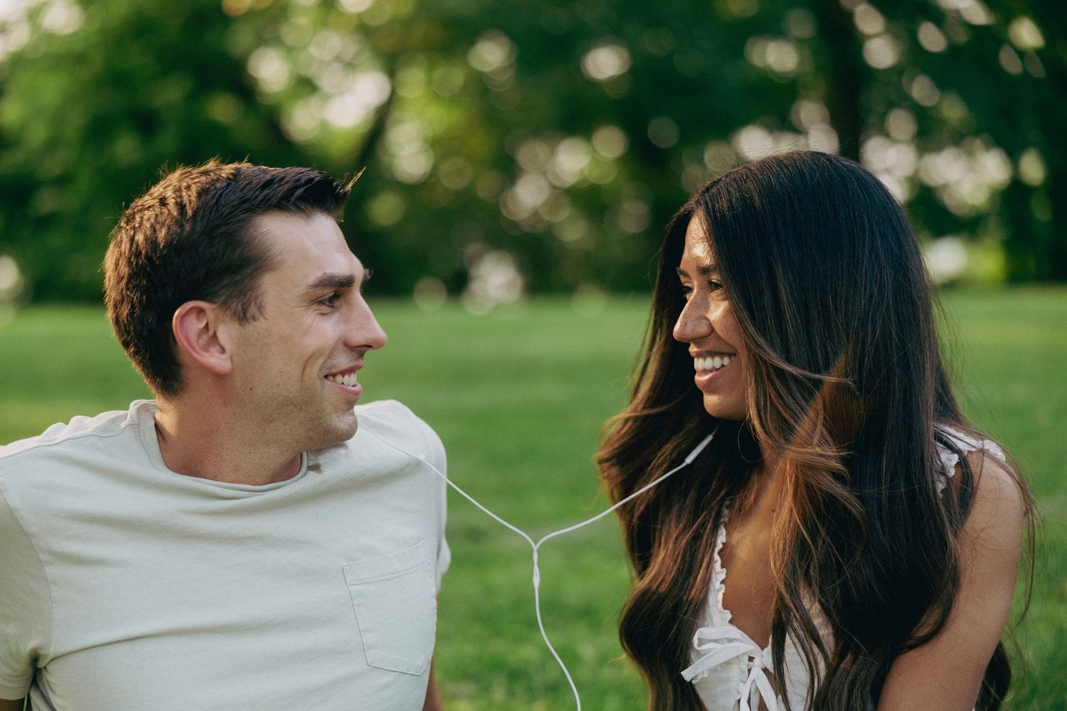 Couple laughing together while sitting on grass in a park.