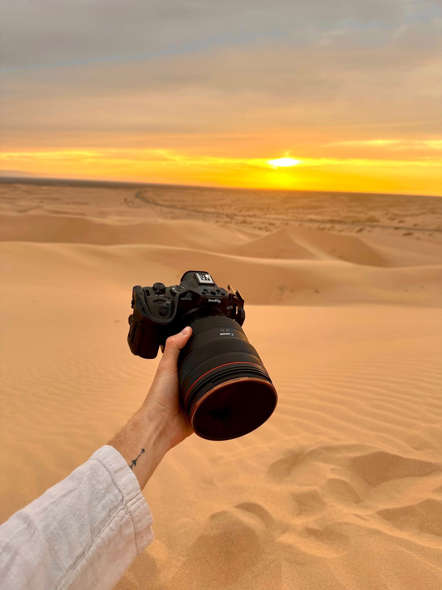 A photographer captures a stunning desert sunset over rolling sand dunes with professional camera equipment.