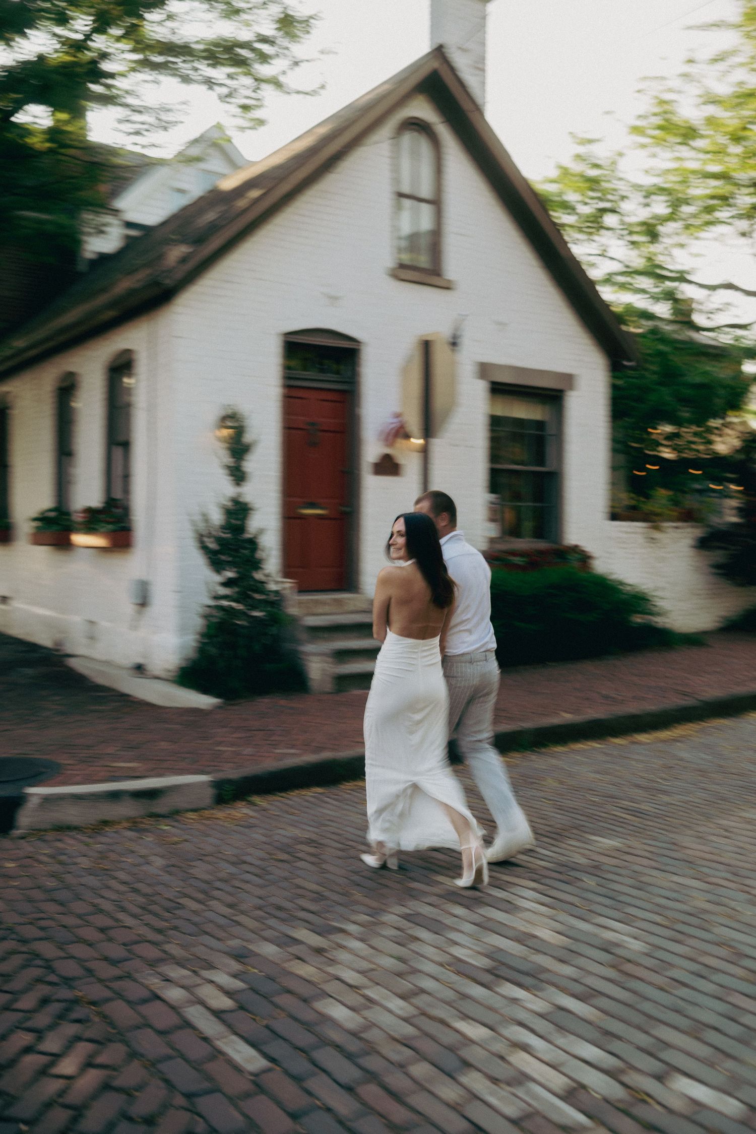 Couple walking along a charming brick street with historic white buildings.