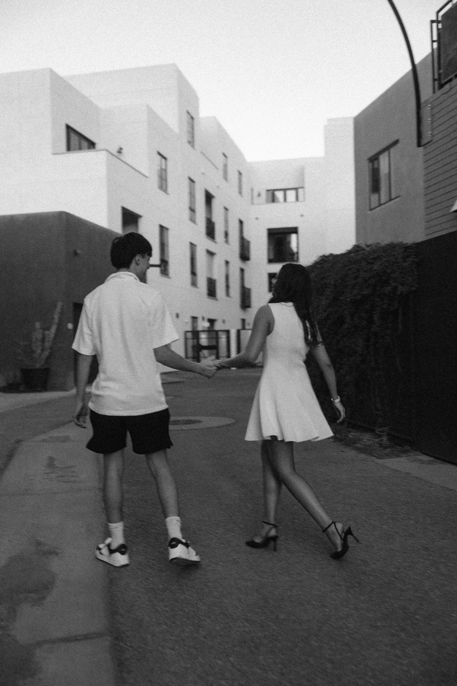 Three black and white photographs show people walking along an urban path between modern buildings.