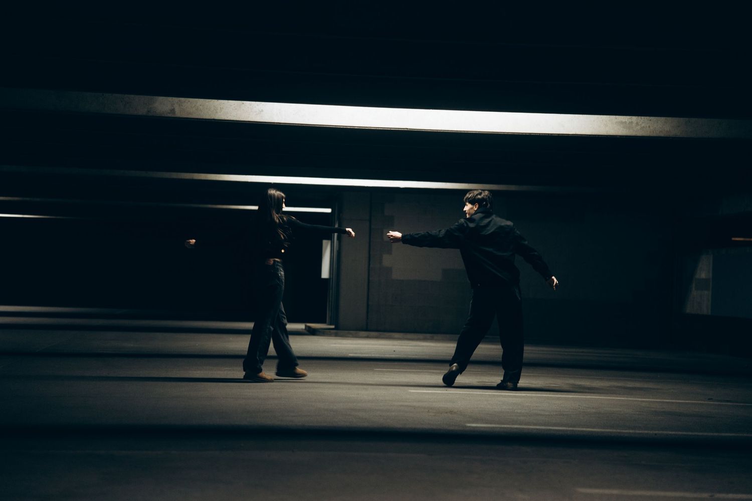 A dark and moody underground parking garage with dramatic lighting and silhouetted figures walking in the distance.