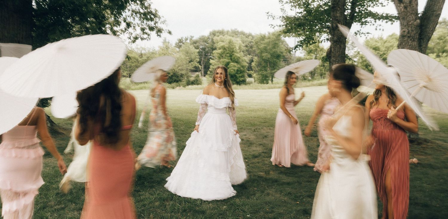 Wedding party in coral and white dresses walking across a lush green lawn.