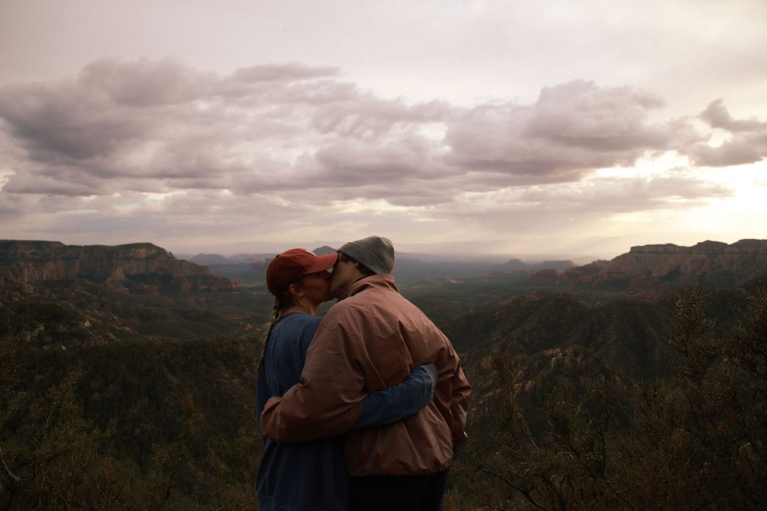 Couple embracing at scenic mountain overlook under dramatic cloudy sky at dusk.